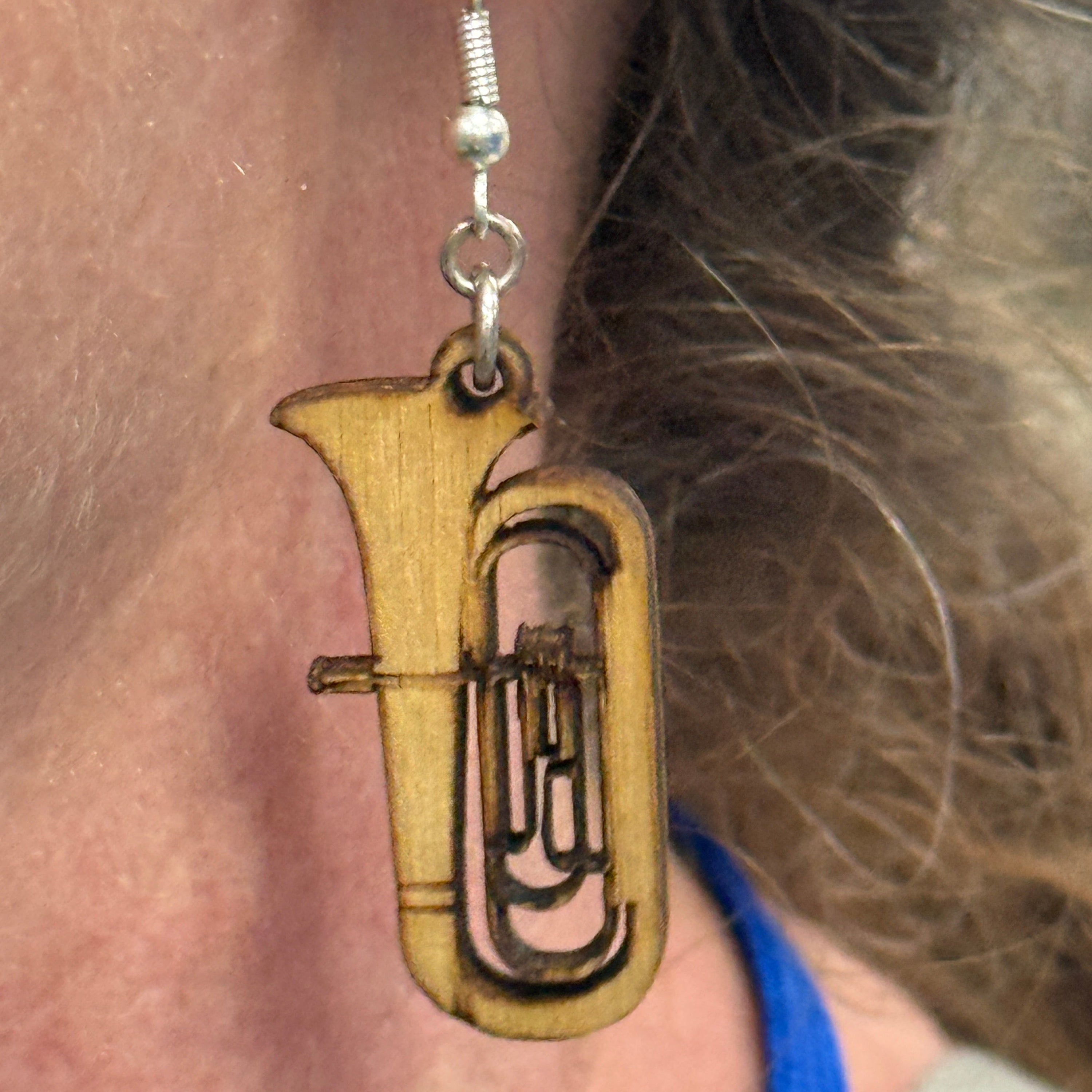 Person wearing a hand-painted wooden tuba dangle earring on a hypoallergenic .925 sterling silver hook, showing the lightweight size, detailed instrument design, and comfortable fit when worn.