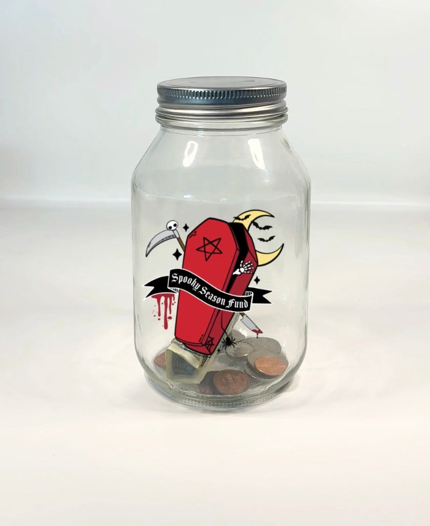 A clear glass mason jar with a silver metal lid, featuring a gothic coffin graphic, with dripping blood, moon, scythe, bats, pentagram, spider, and a moon with the text &