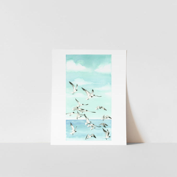 A framed art print featuring a watercolor painting of birds in flight over a body of water, presented against a white background.