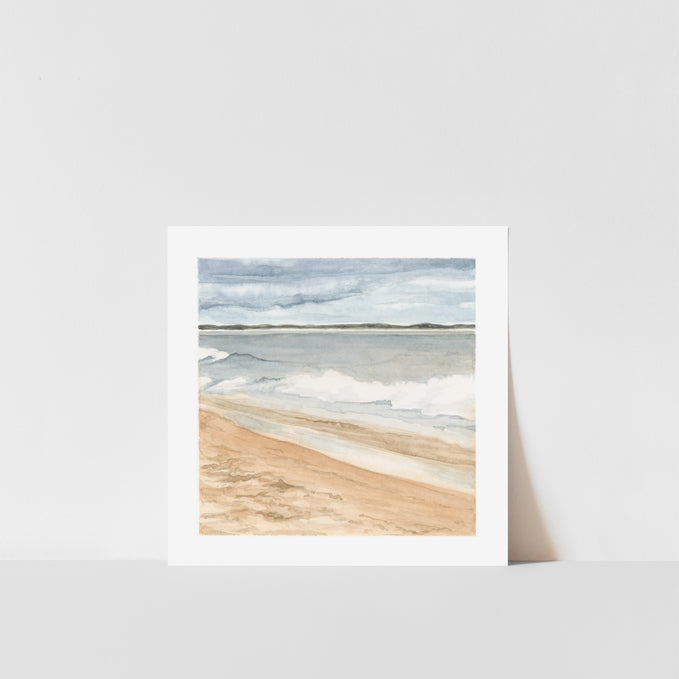 A framed art print featuring a watercolor painting of a coastline scene with sand, sea, and sky.