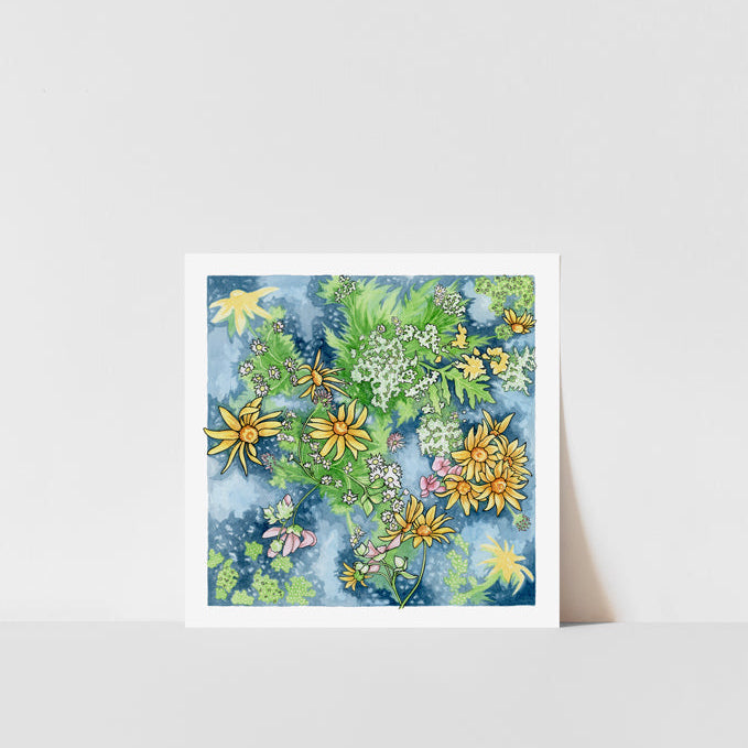 A framed art print featuring a watercolor painting of wildflowers with a blue background, displayed on a white shelf against a white wall.
