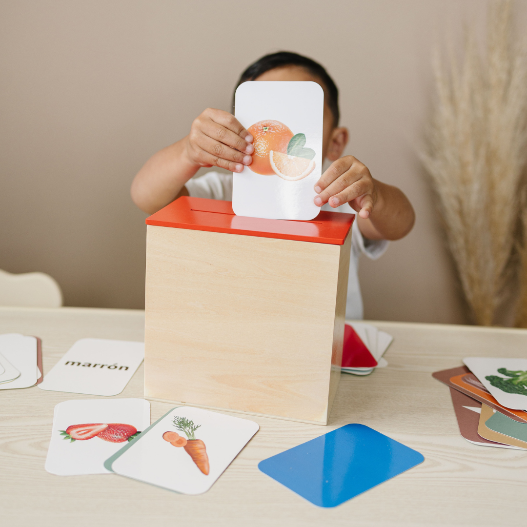 Child playing with a educational toy that has cards and a wooden box on a table.