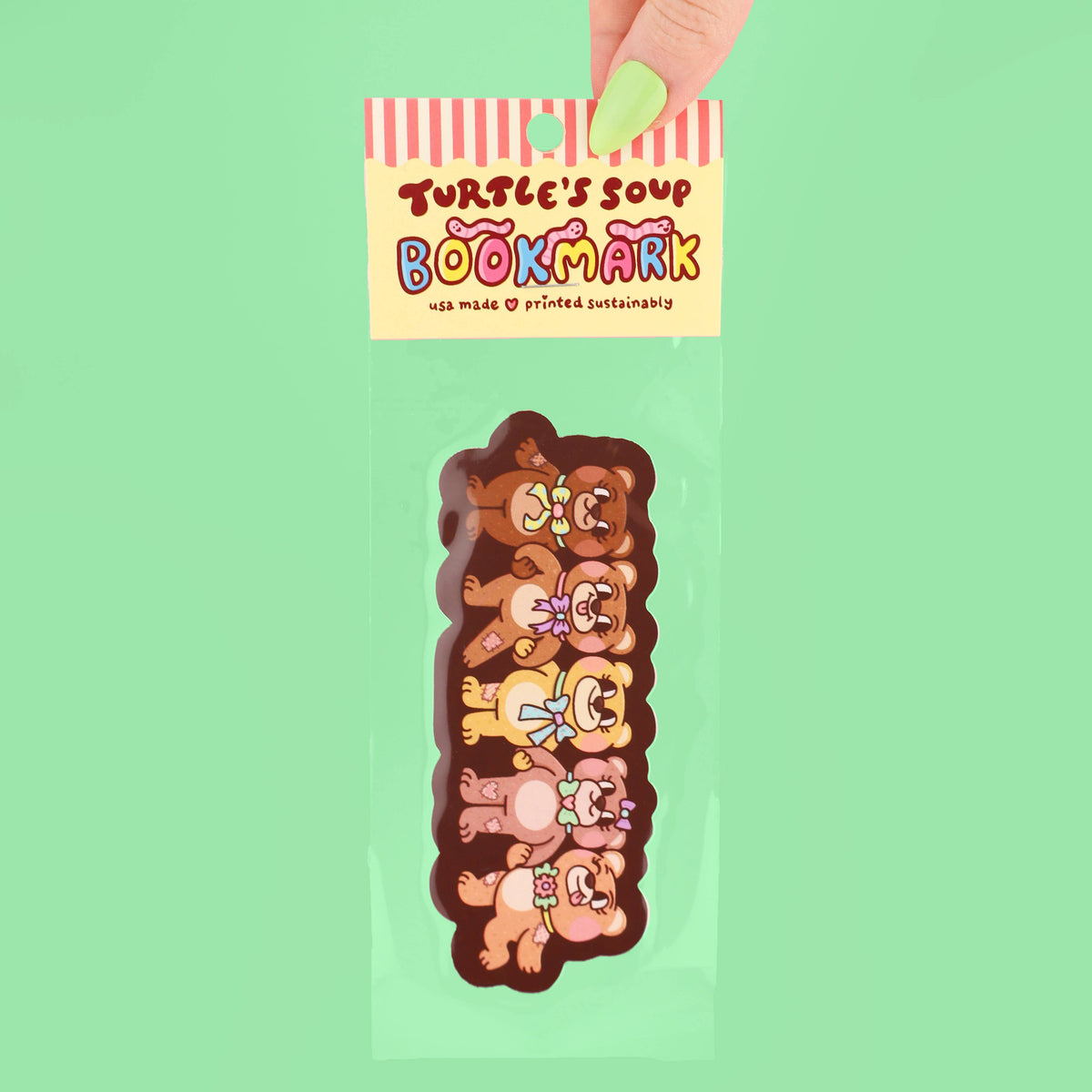 Bookmark with cartoon teddy bear design held by a hand against a green background