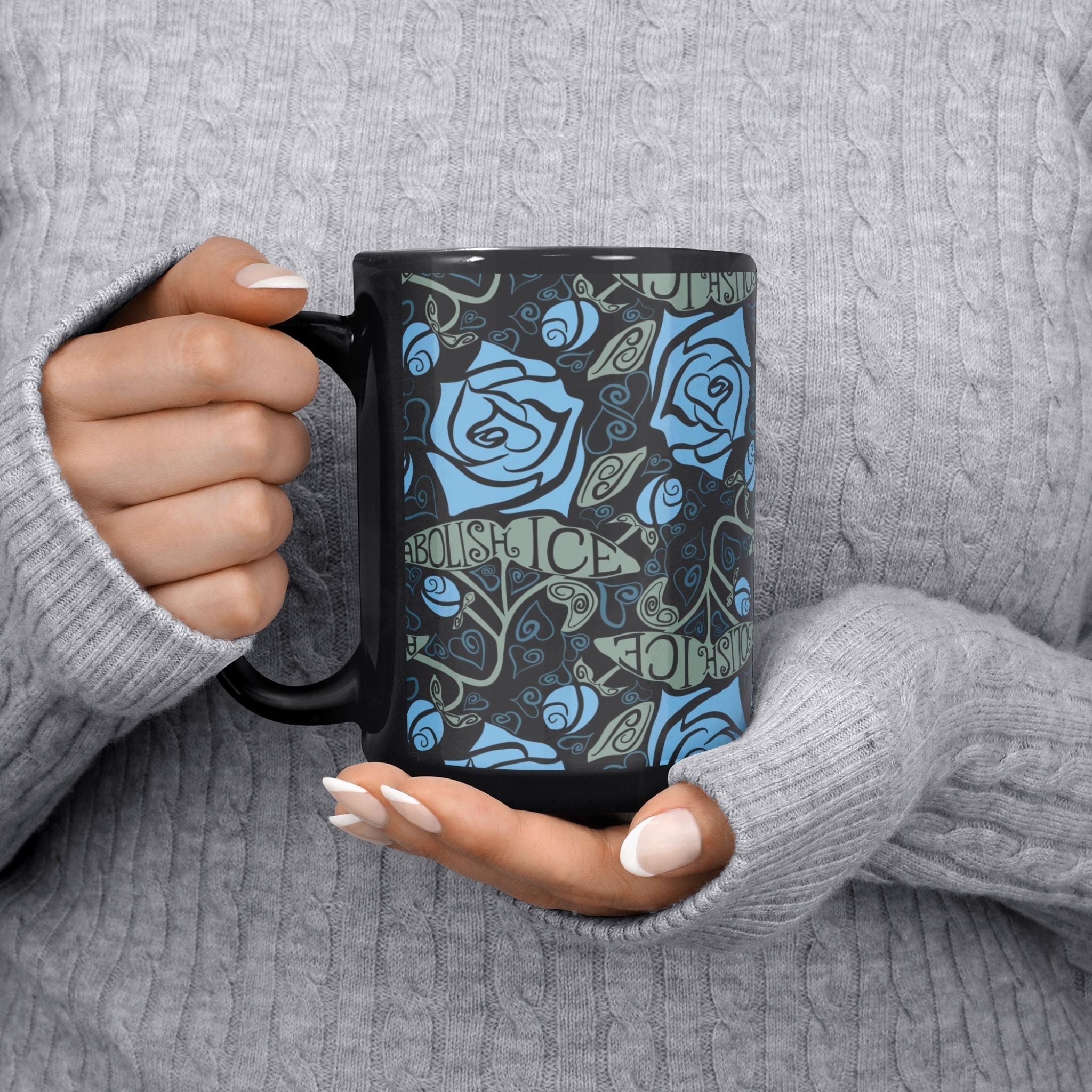 Person in grey cable-knit sweater holding the Abolish ICE black ceramic mug, 15oz gothic rose wrap print visible
