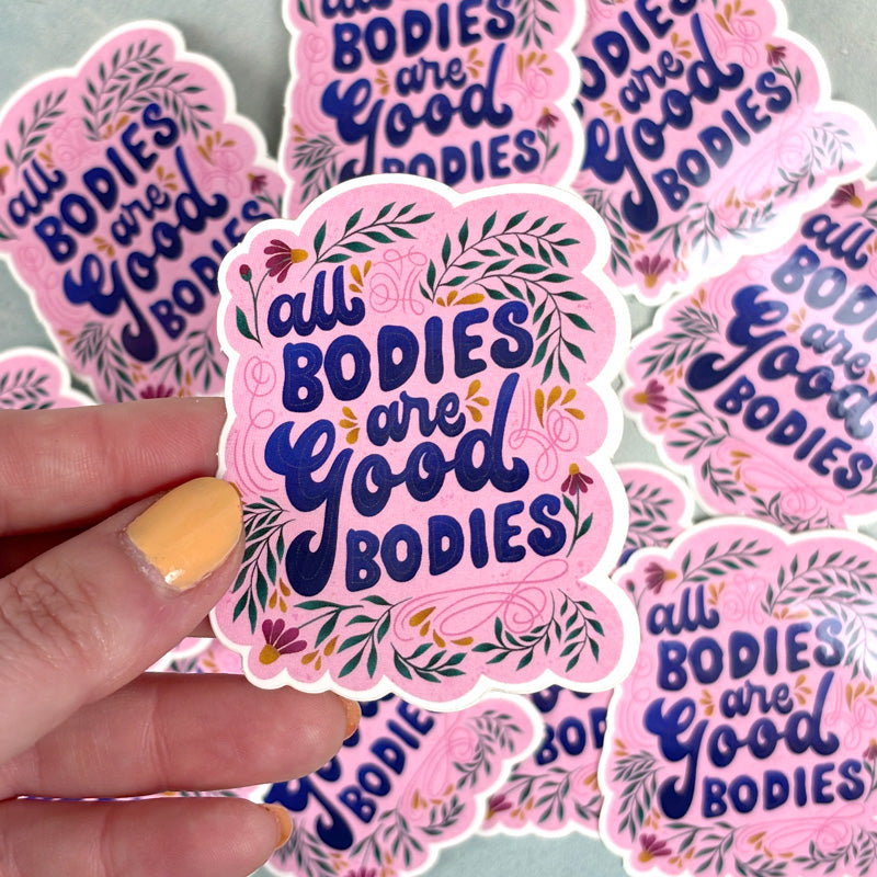 hand holding A sticker with a pink background and a green floral pattern, featuring the text &