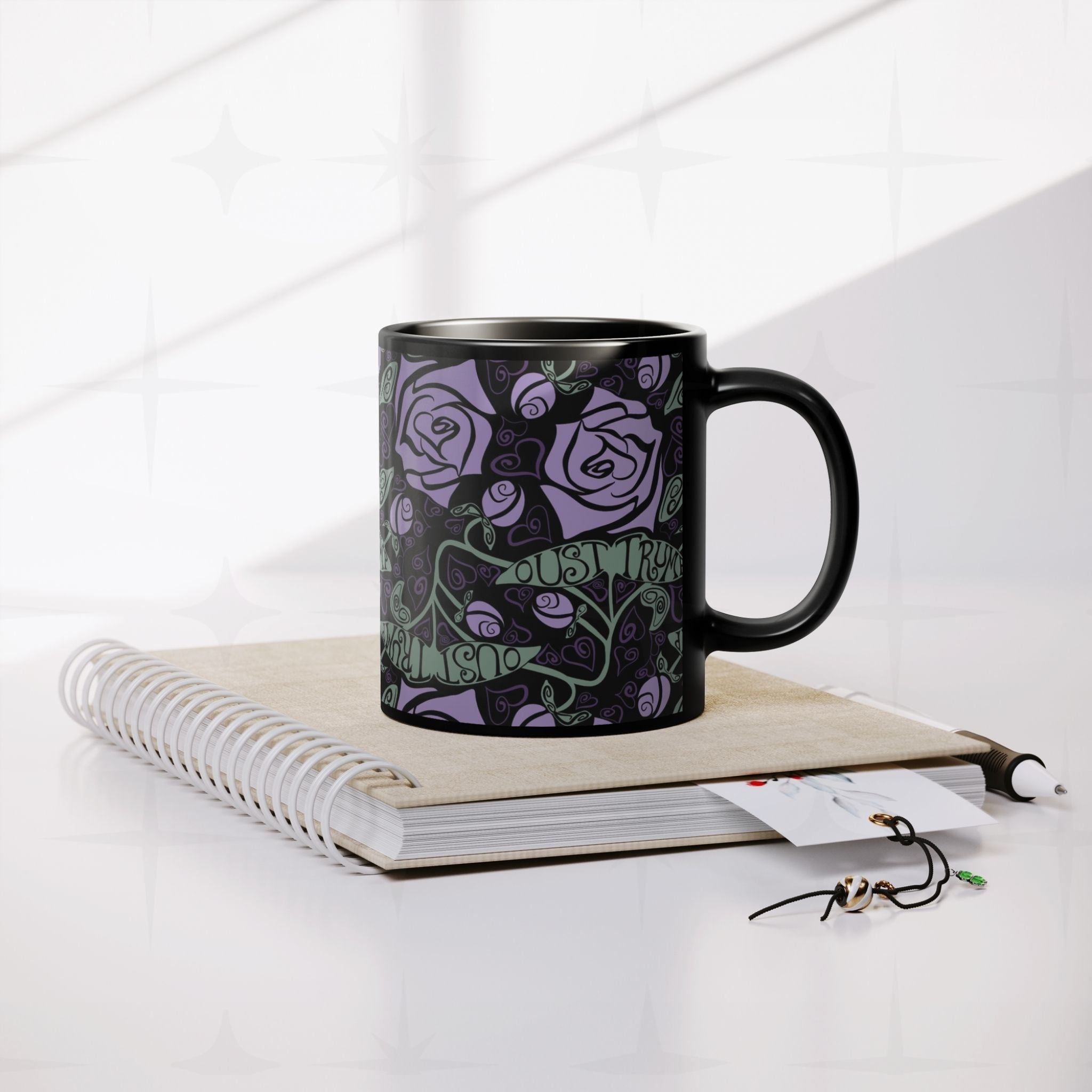 Anti-Trump hidden message black ceramic mug resting on spiral notebook with pen and accessories