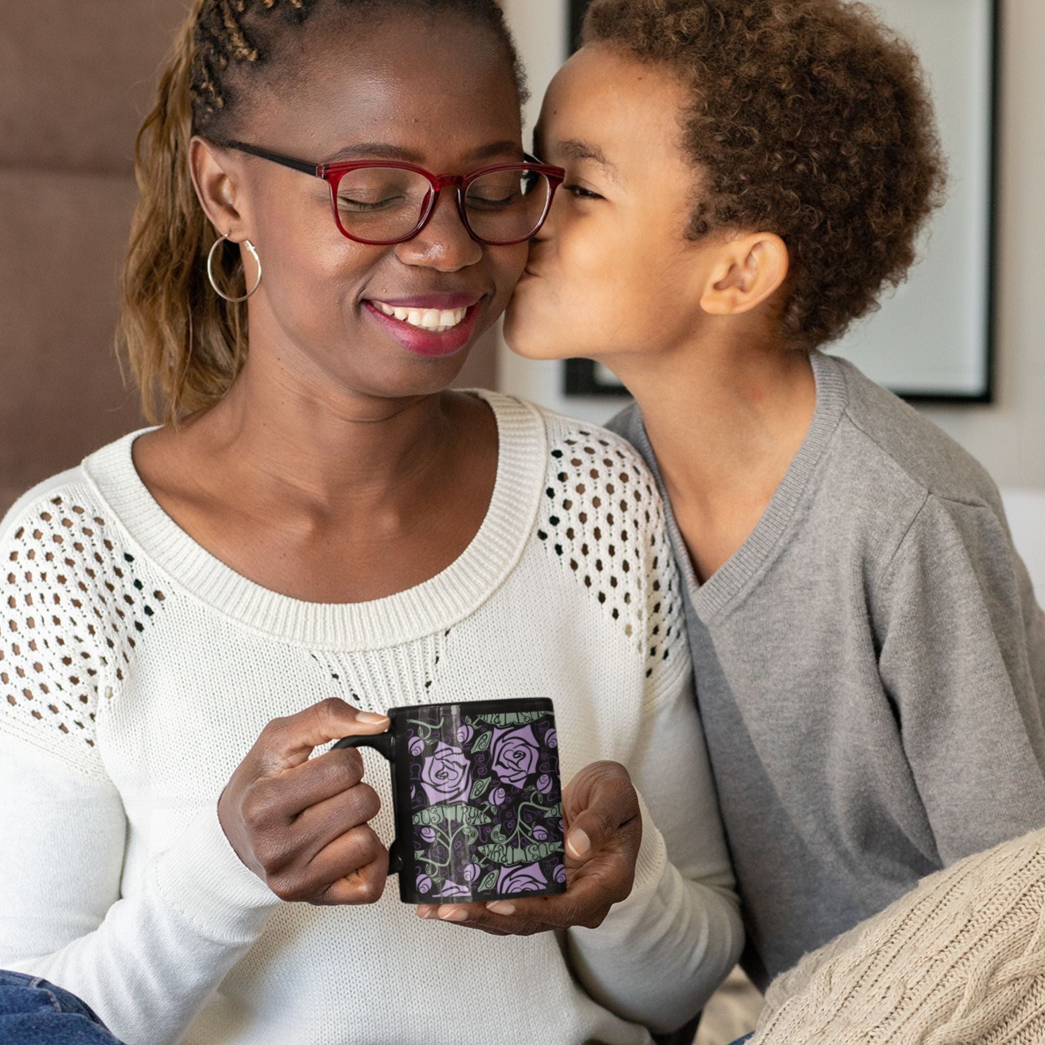 Woman smiling and holding anti-Trump floral gothic coffee mug while child gives her a kiss on the cheek