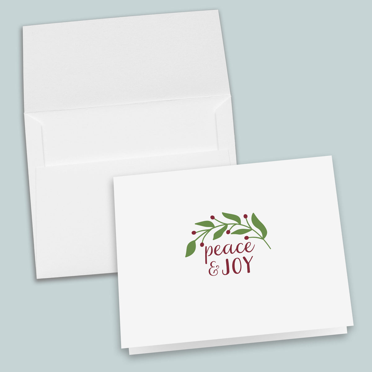 a white greeting card with a peace and joy message, along with a decorative leaf and berry design.