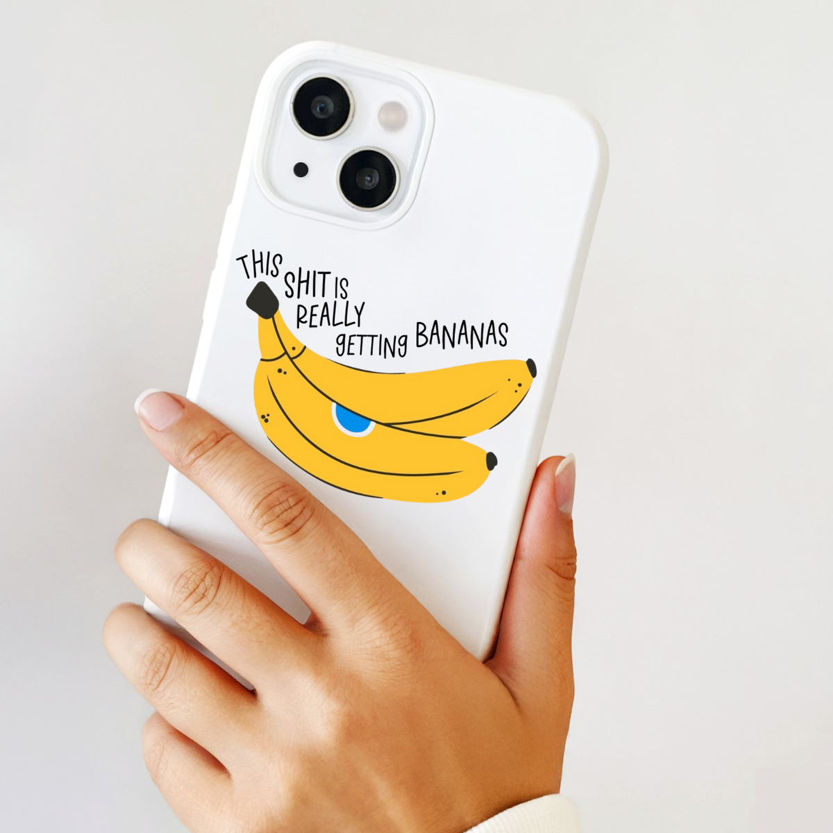 Phone case with banana illustration and text held by a hand on a light background