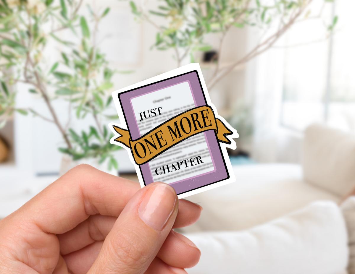 A hand holds a die-cut sticker shaped like a book chapter, featuring a purple border, white page background, and a gold ribbon banner that reads &