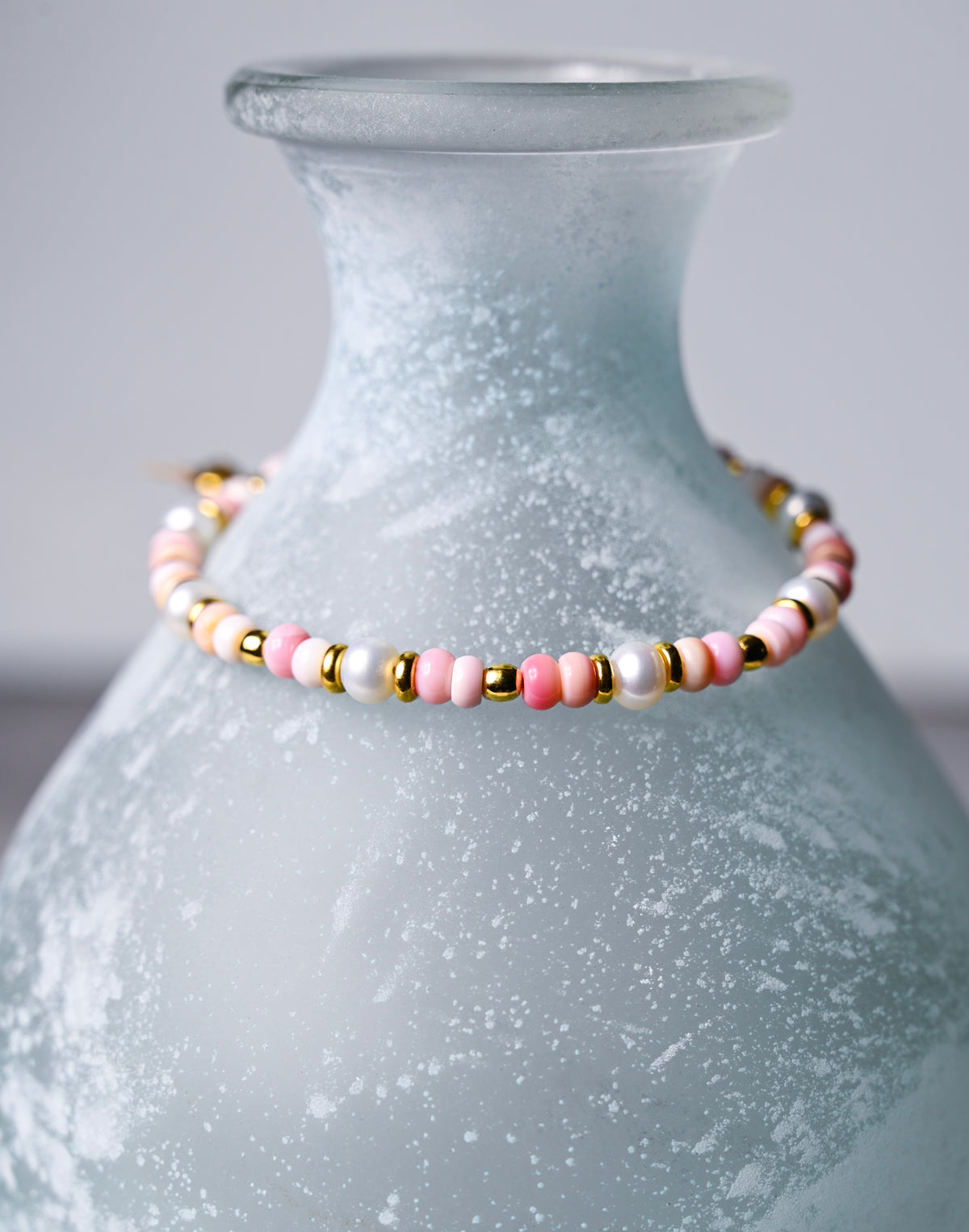 A closeup view of a pink shell bracelet with gold accents.