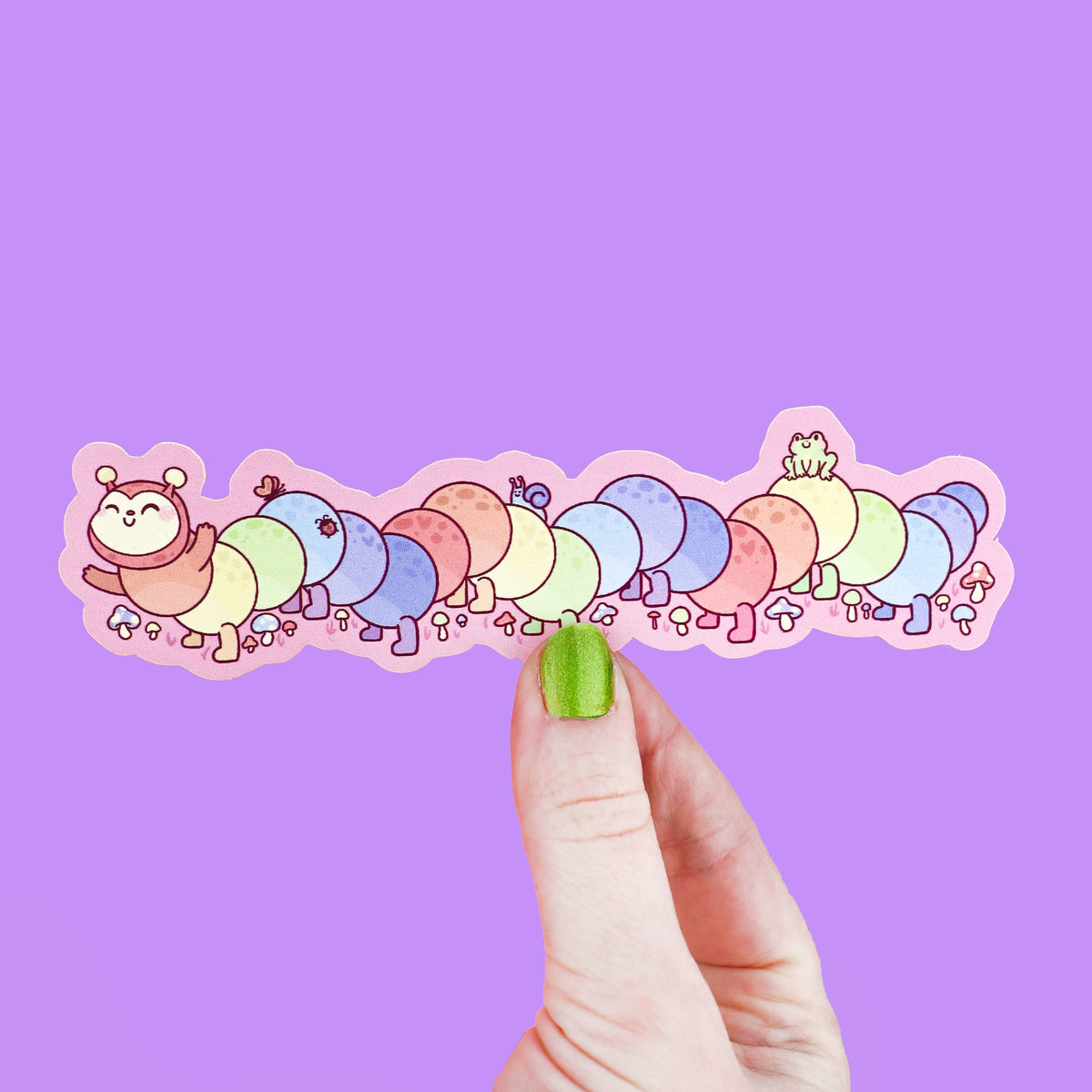 Colorful caterpillar bookmark held by a hand against a purple background