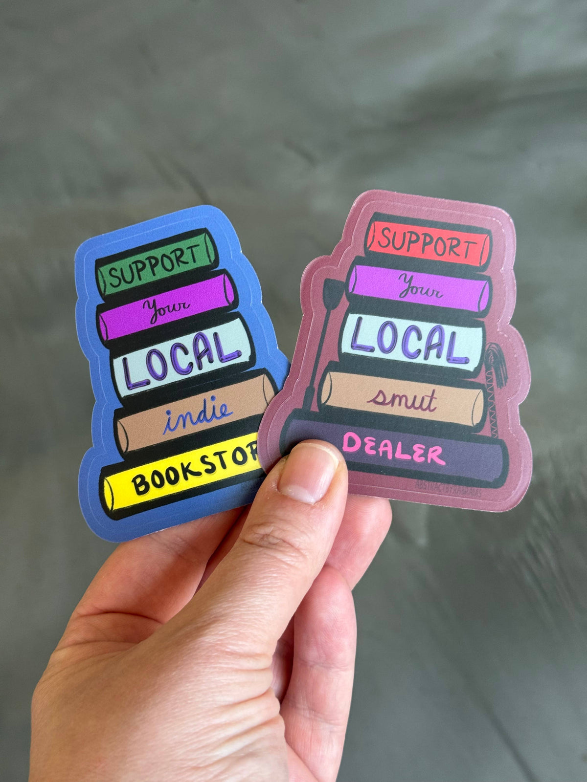 Two colorful stickers held by a hand with a gray background