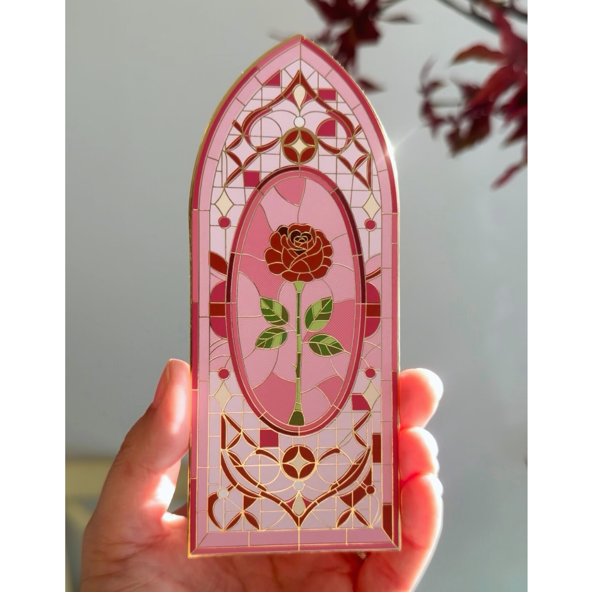 Decorative bookmark with a rose design held in a hand against a neutral background