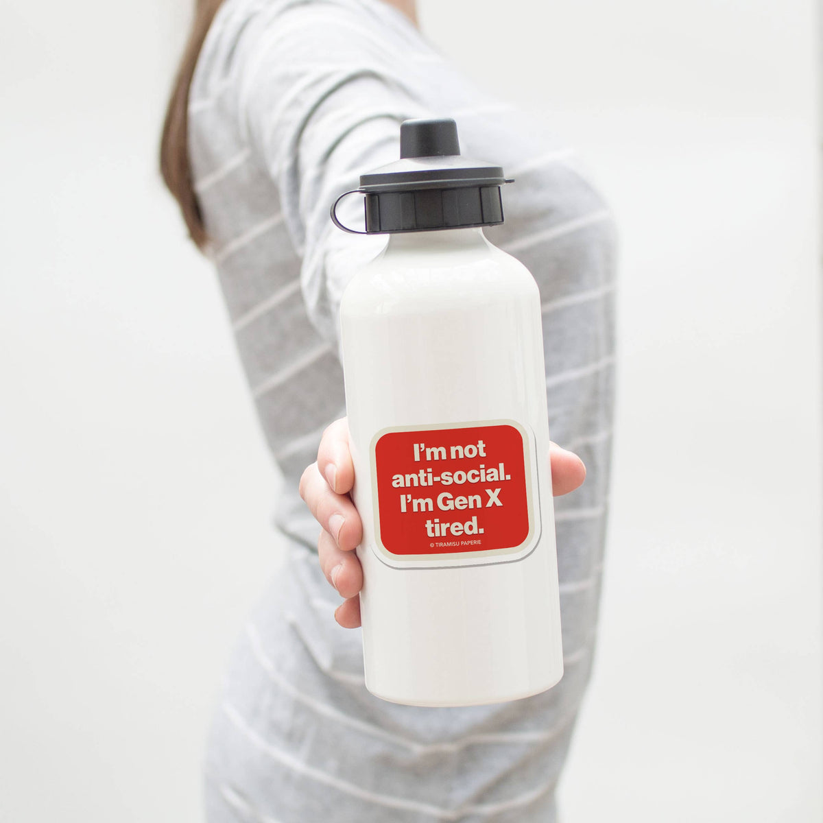 Person holding a white water bottle with a red sticker on a plain background