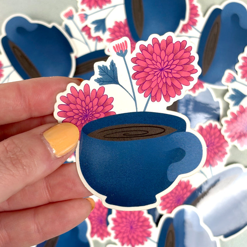 hand holding sticker of a blue coffee mug with pink flowers