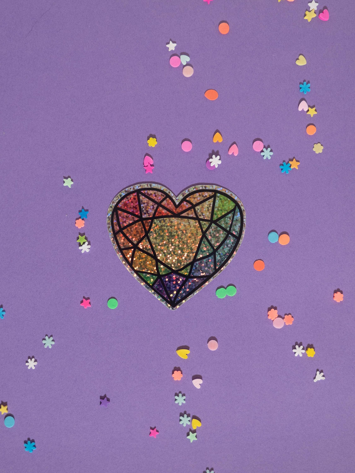 Colorful heart design on a purple background with confetti-like shapes.