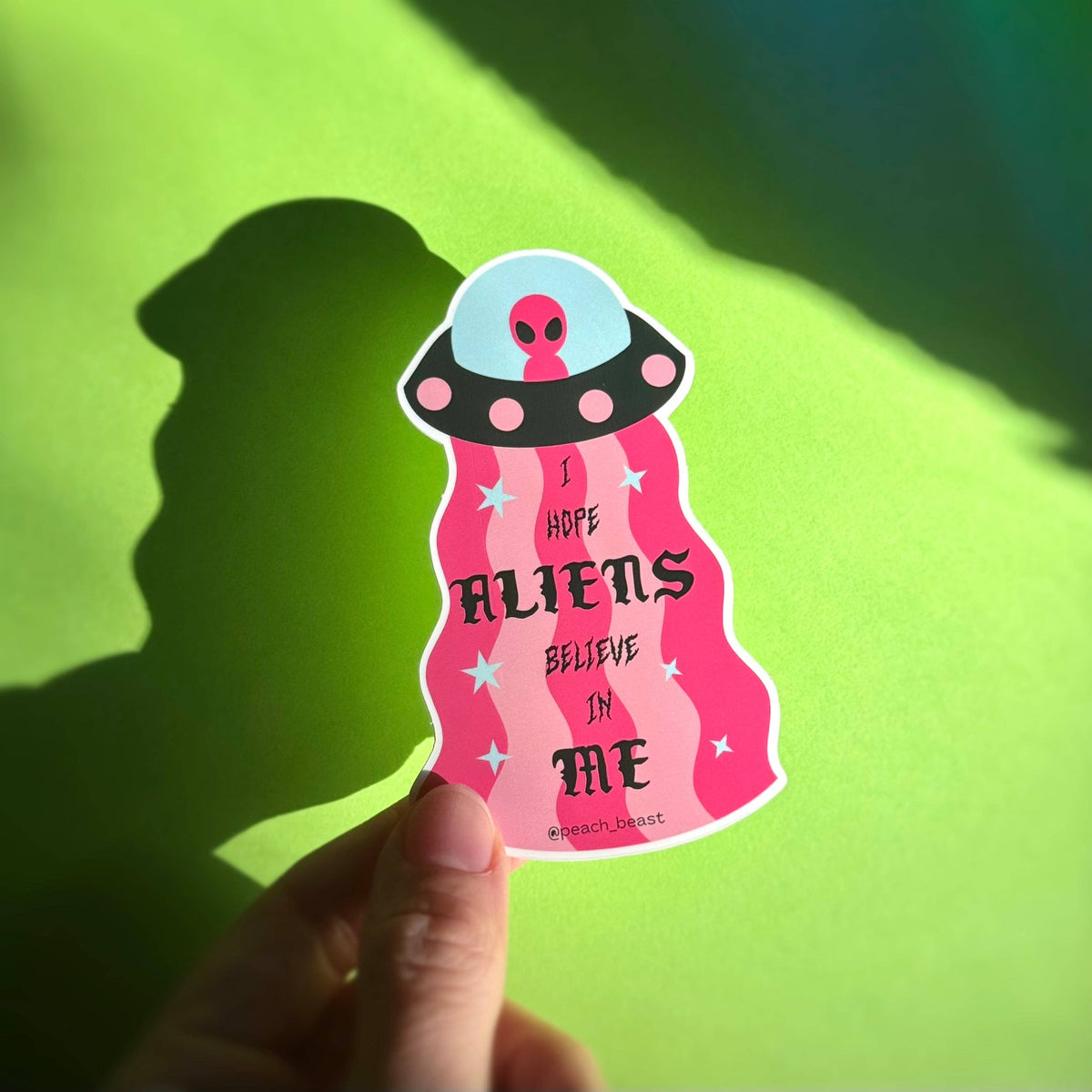 Sticker with alien design and text held against a green background