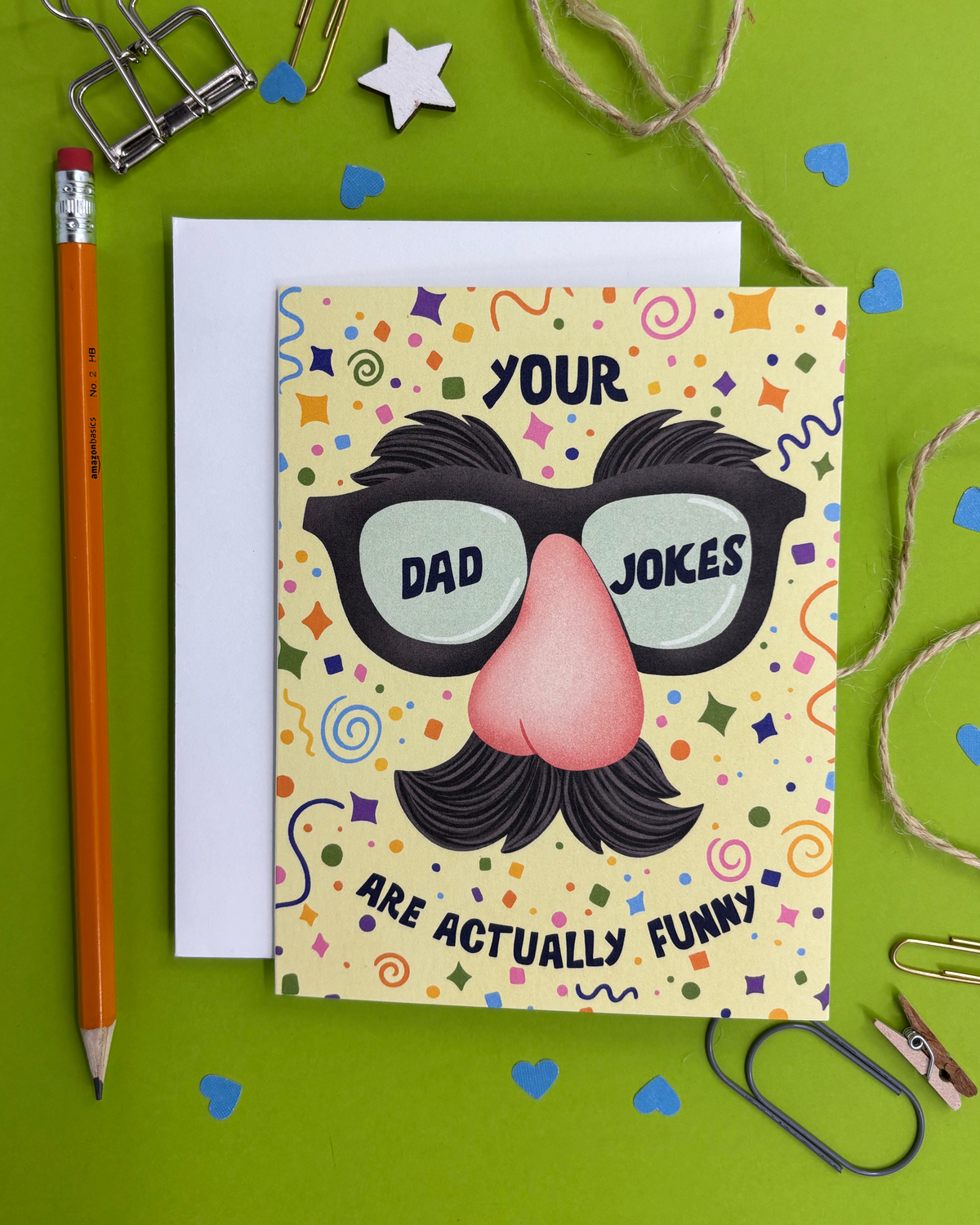 Card with a humorous design of glasses, mustache, and text on a green background with stationery items.