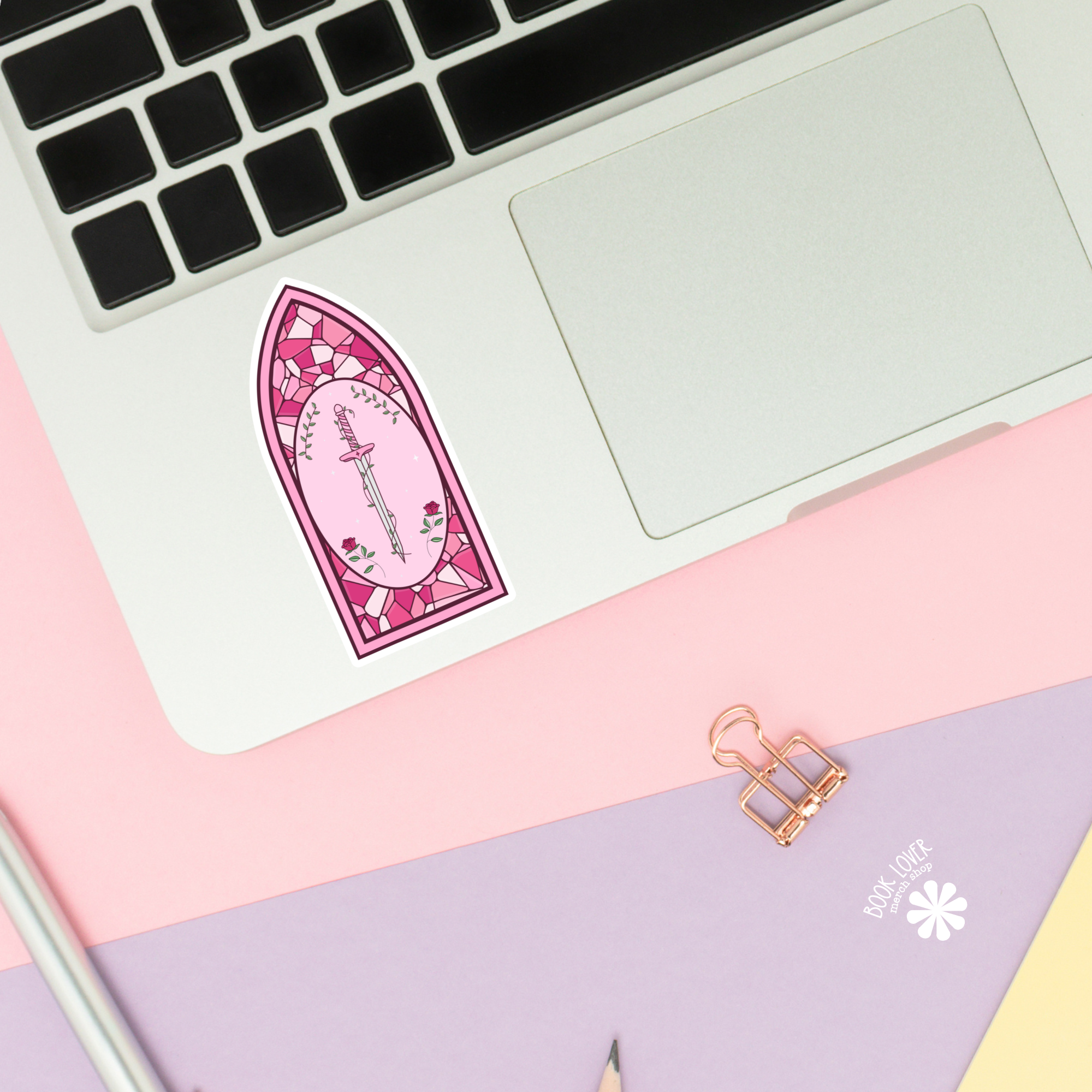 Pink fairy door sticker on a laptop with stationery items on a pink and purple surface