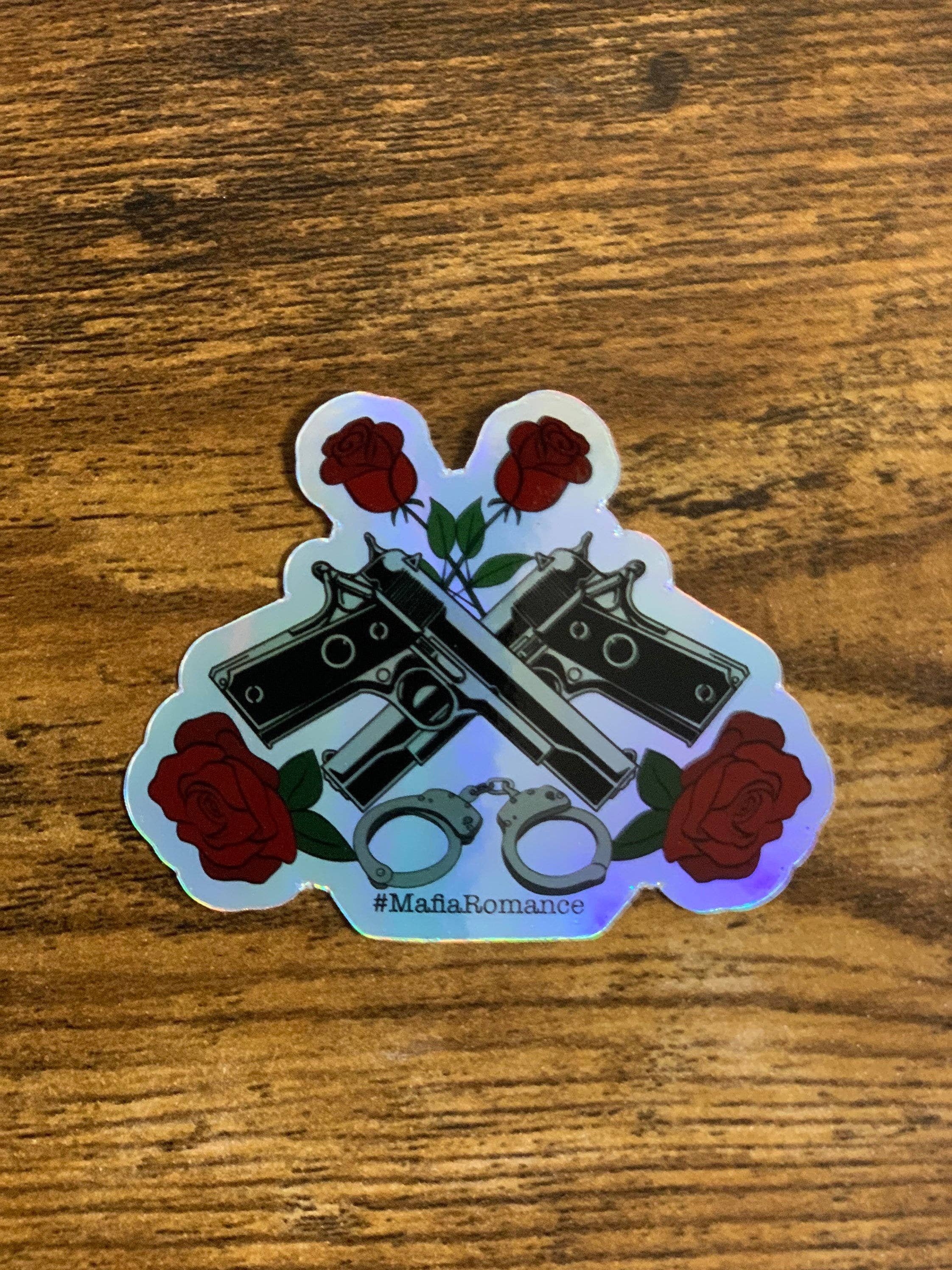 Sticker with crossed revolvers, handcuffs, and roses on a wooden surface
