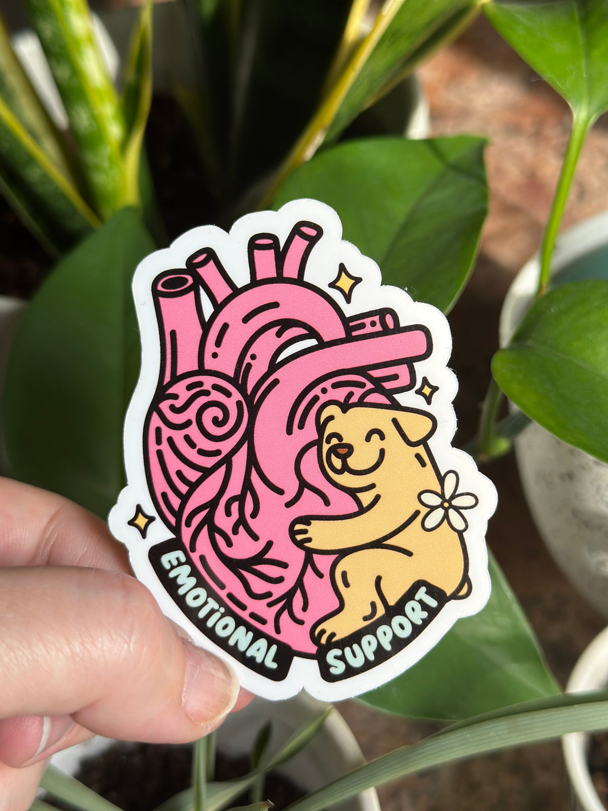 A hand holding a sticker with an illustration of a dog and a heart, with the text &
