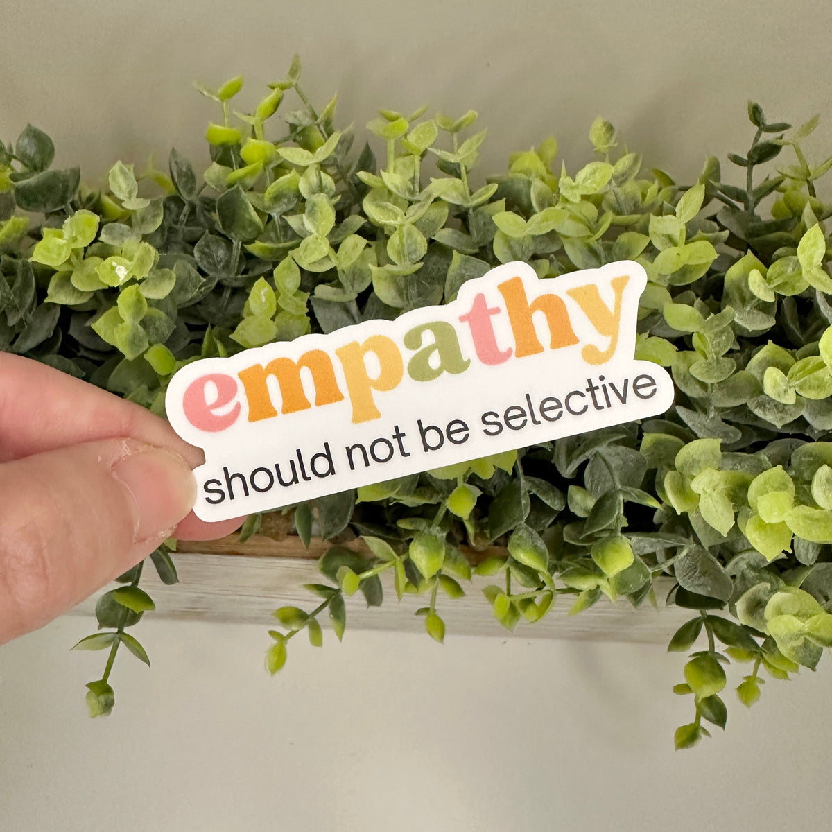 Hand holding a pro-empathy sticker text in front of plant