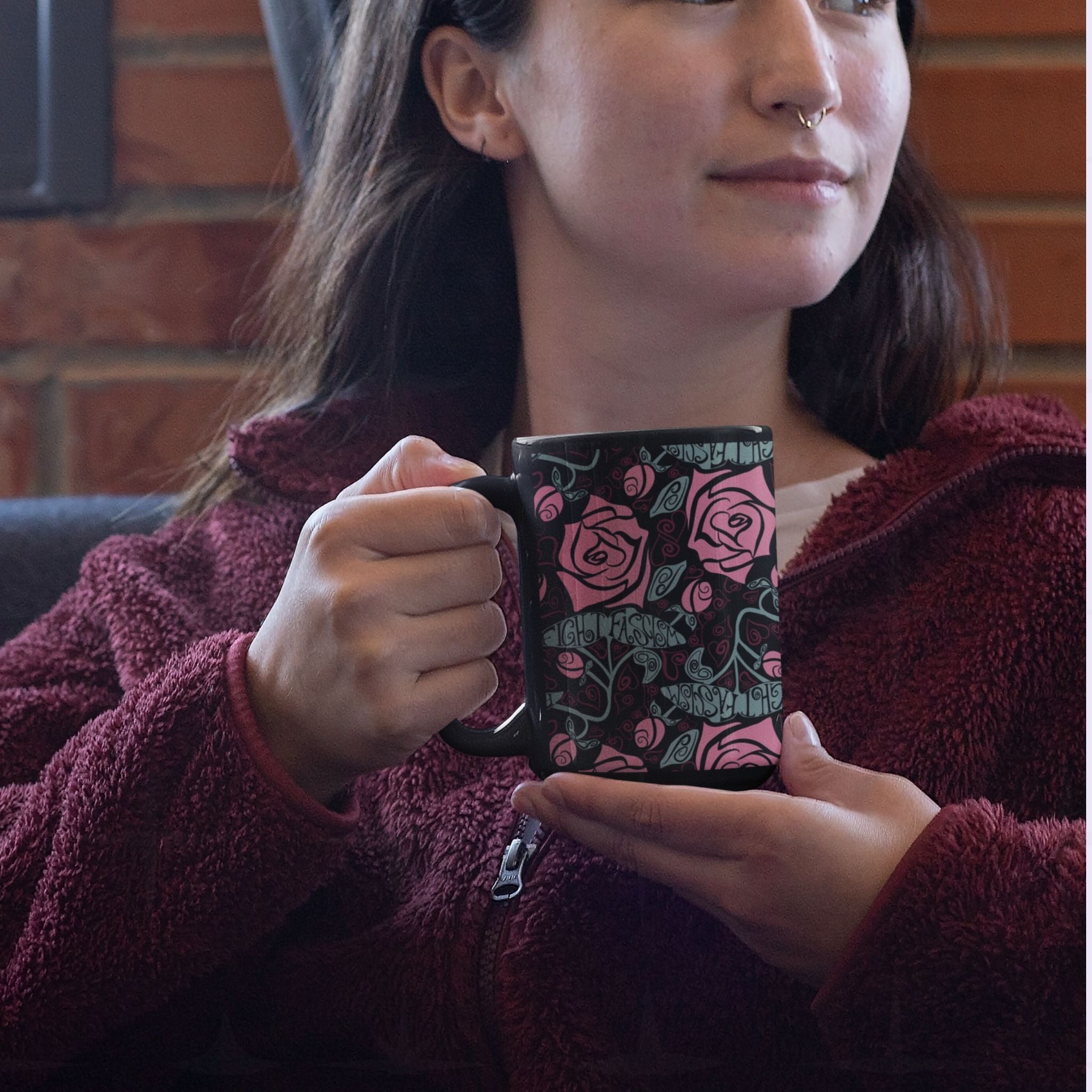 Woman holding a dark floral hidden message coffee mug featuring salmon pink roses and a hidden activist message "fight fascism" woven into the botanical pattern on a glossy black ceramic mug