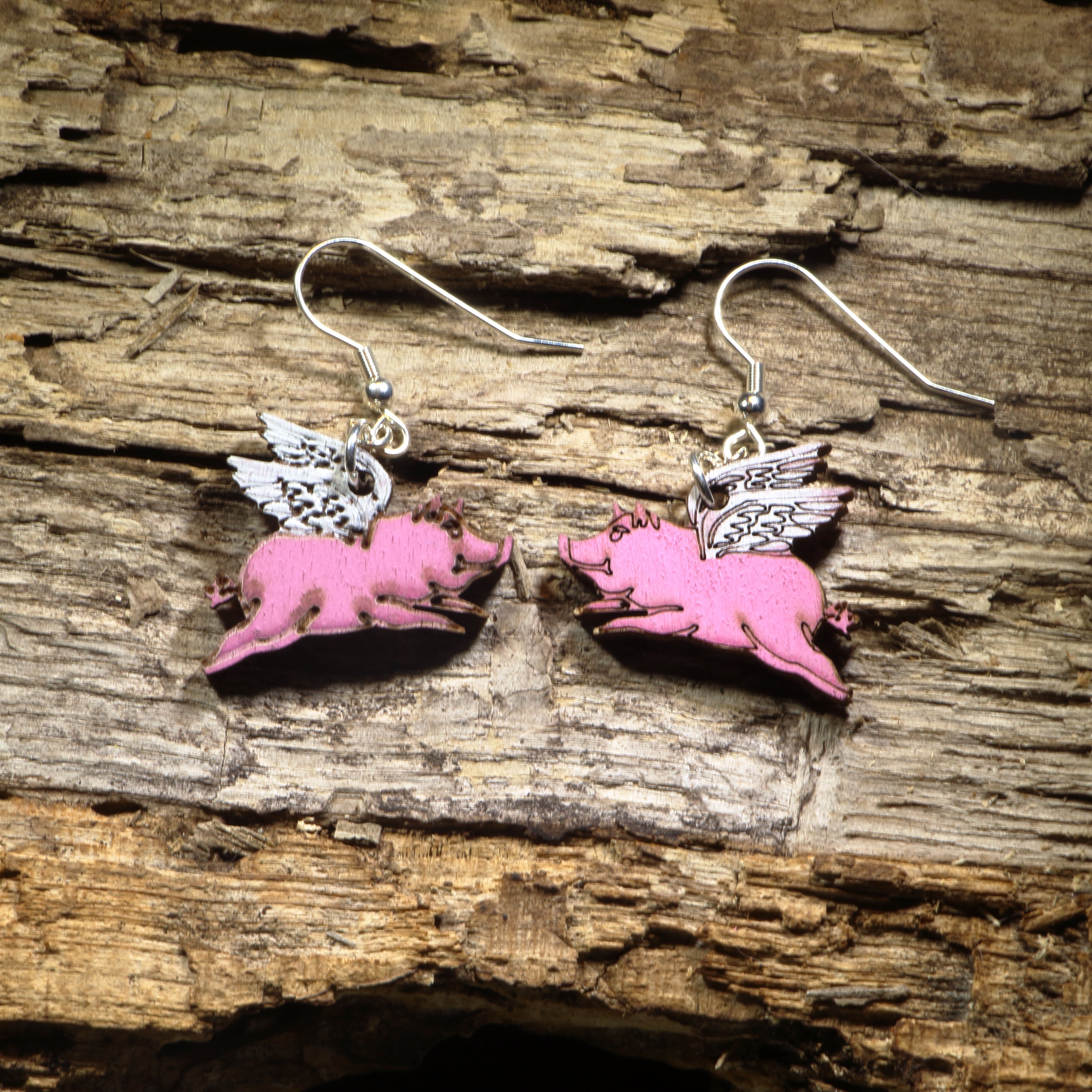 Hand-painted wooden flying pig dangle earrings featuring adorable pink pigs with detailed white wings. Crafted from lightweight wood with hypoallergenic .925 sterling silver hooks, these whimsical earrings are perfect for pig lovers, farm animal fans, fantasy enthusiasts, and anyone who enjoys quirky, humorous jewelry that proves anything is possible when pigs fly.