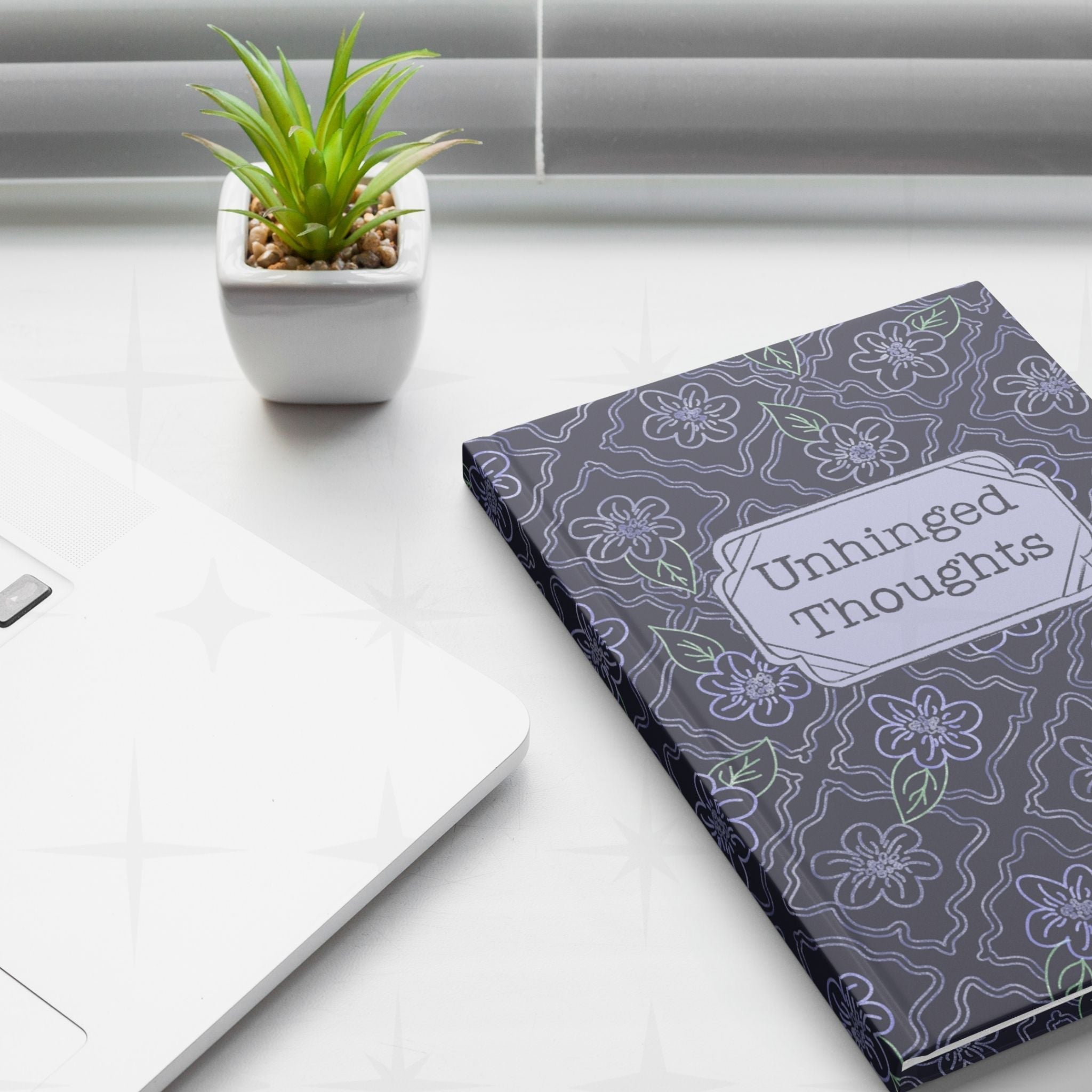 Gothic lavender floral journal on white desk next to laptop and small succulent plant, minimalist workspace