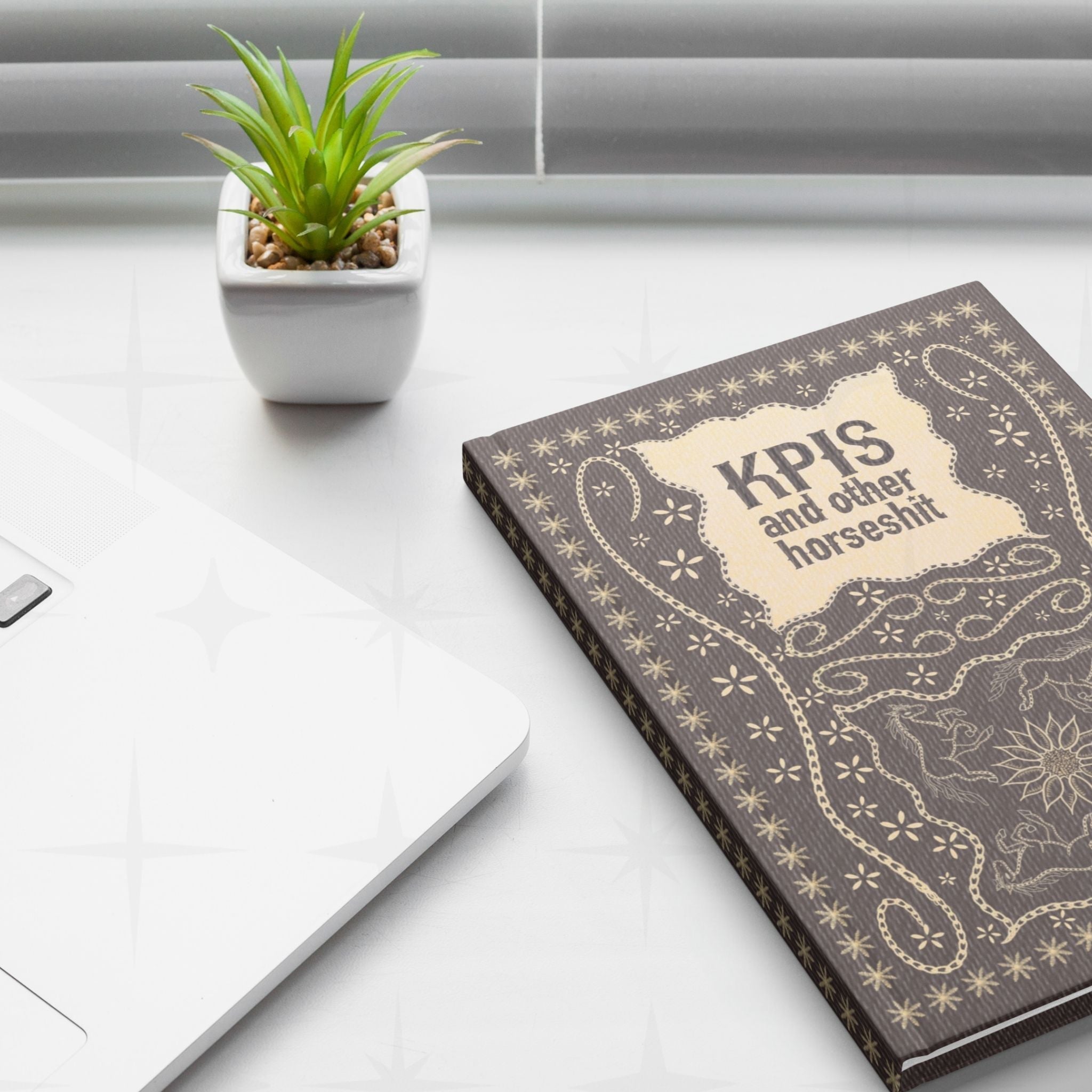 Funny KPI profanity journal on white desk next to laptop and small succulent plant in work from home lifestyle setting