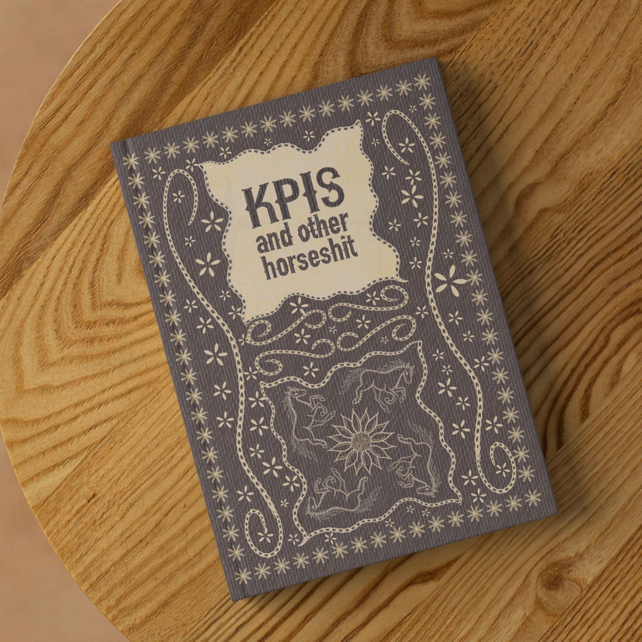 KPI profanity hardcover journal with vintage equestrian design lying on round wooden surface showing front cover
