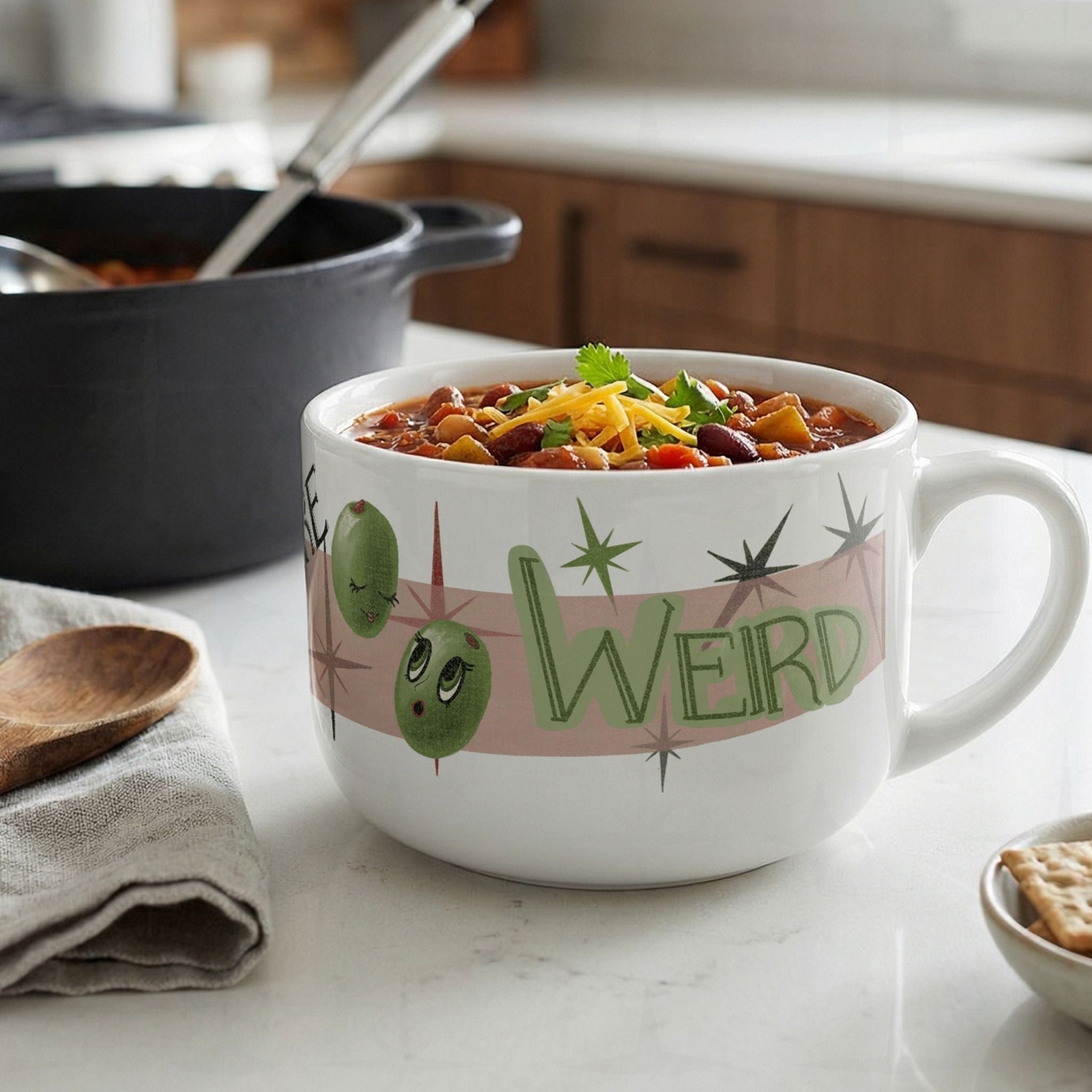 Large 25oz ceramic funny mom latte mug filled with chili and shredded cheese on white marble kitchen counter, retro Weird olive pun design with illustrated olive characters visible