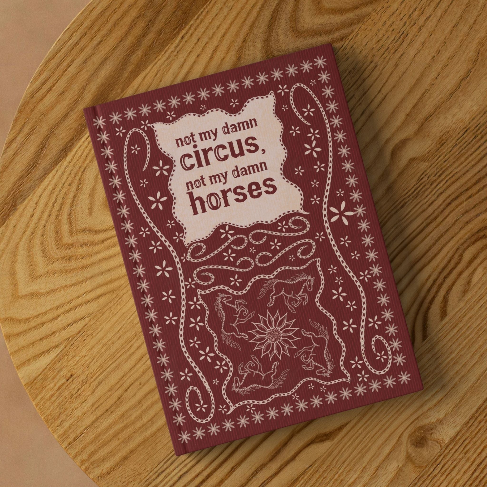 Funny western hardcover journal lying on round wooden surface showing front cover with stitched leather folk art design