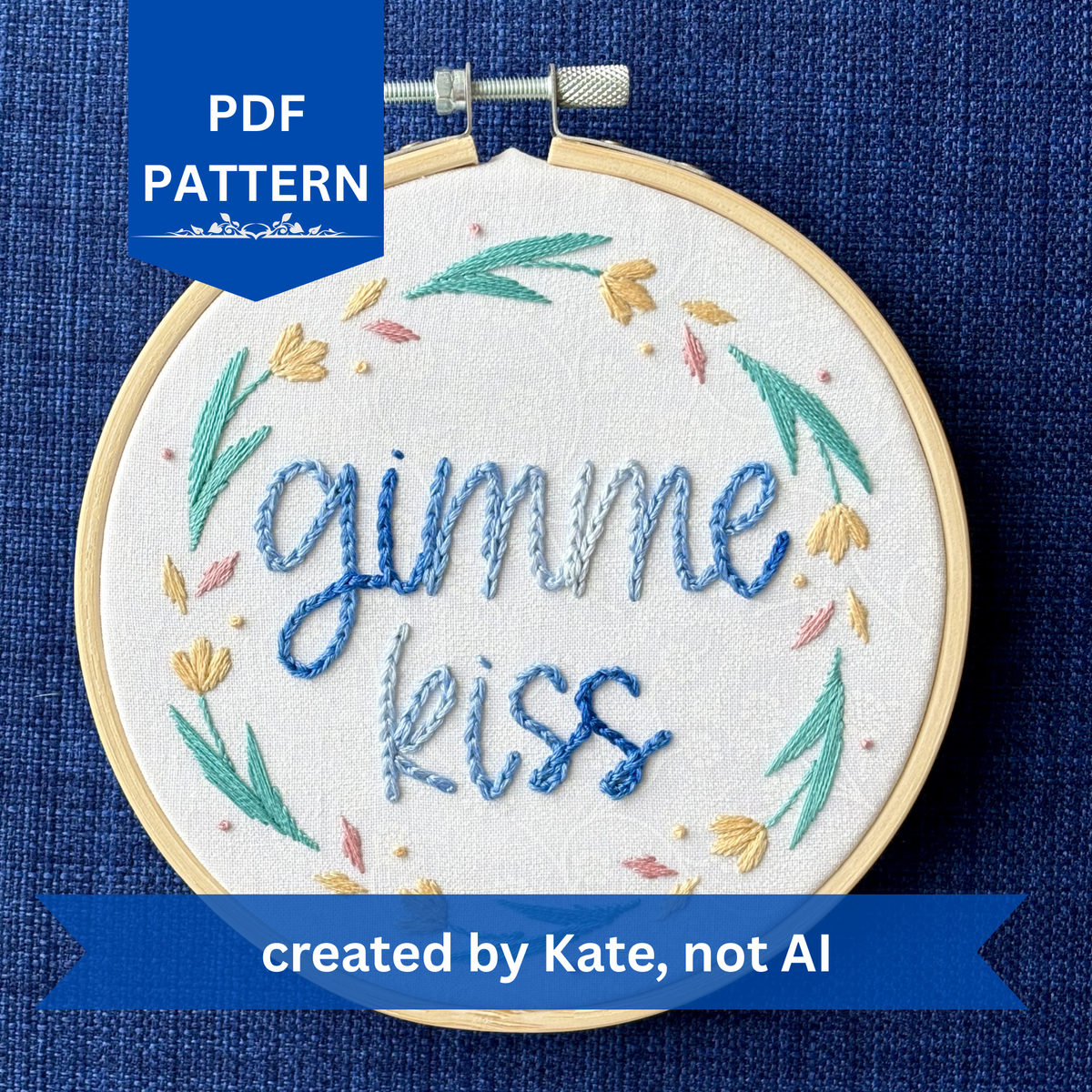 PDF pattern created by Kate, not AI. "Gimme kiss". Quote hand embroidered in handwriting font in variegated blues. Surrounding the text is a floral wreath with pastel yellow flowers, green stems and leaves, and yellow and pink floating petals. Sewn on white-on-white cotton. Framed as wall art in a light wood embroidery hoop.