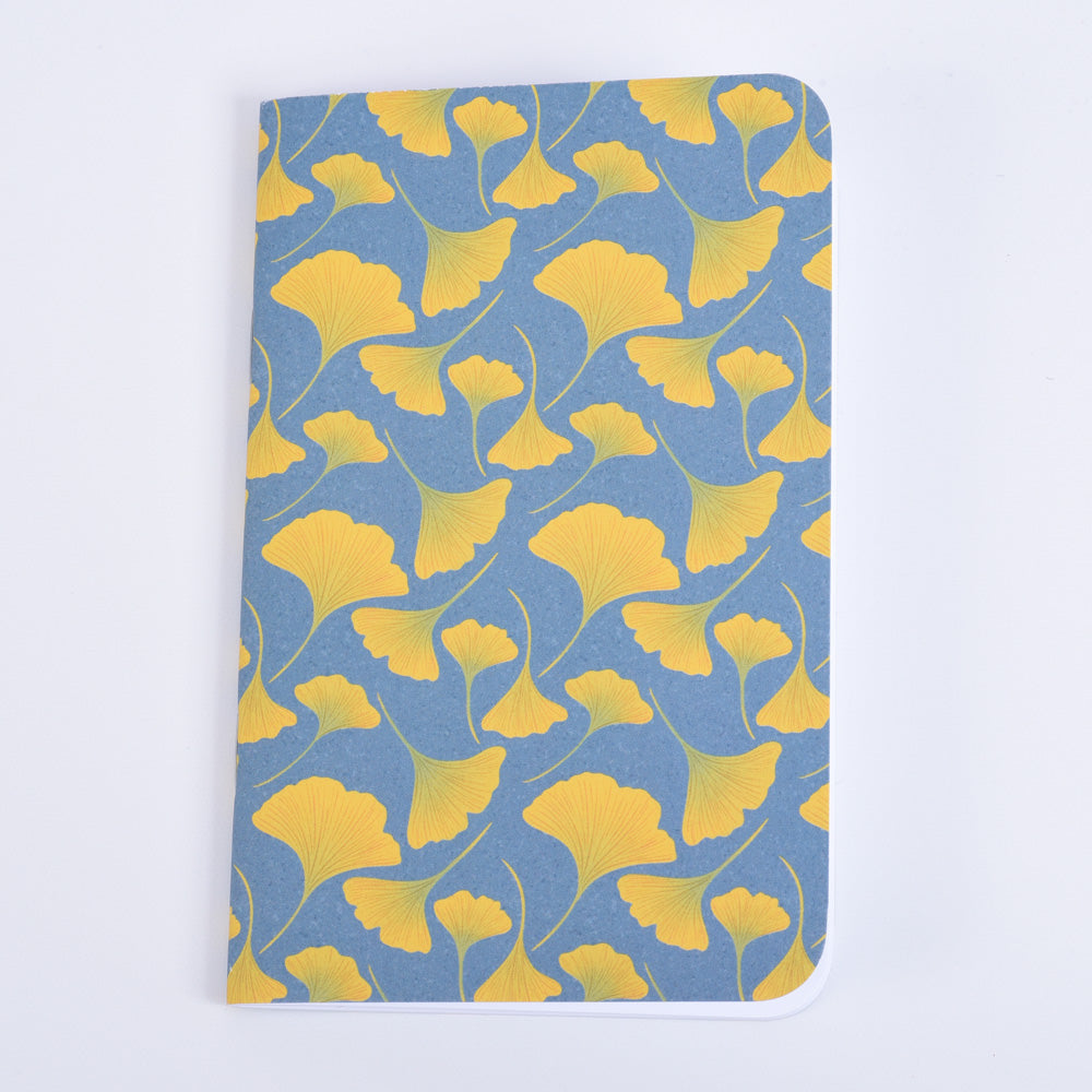 A pocket notebook with a blue background featuring a yellow floral pattern of gingko leaves.