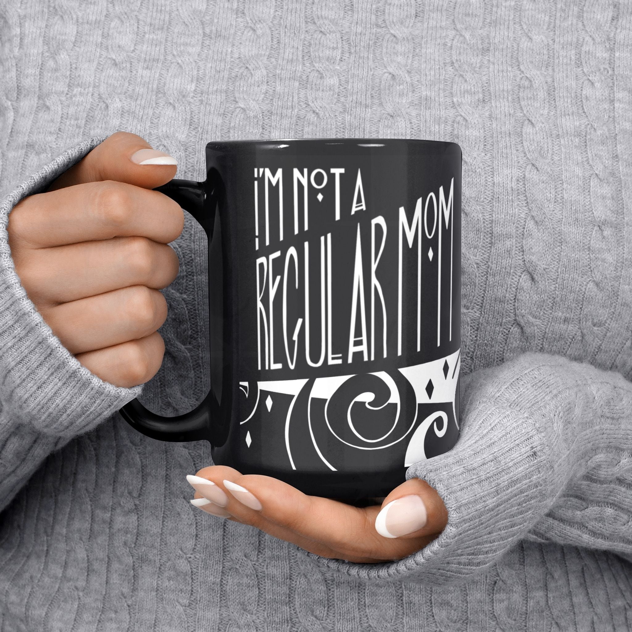 Person in grey cable-knit sweater holding black goth mom mug showing I&