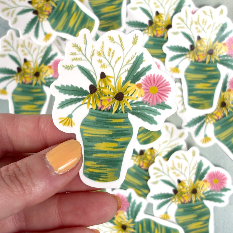 hand holding A sticker with a floral design featuring a bouquet of flowers in a green vase, highlighted with watercolor-like colors.