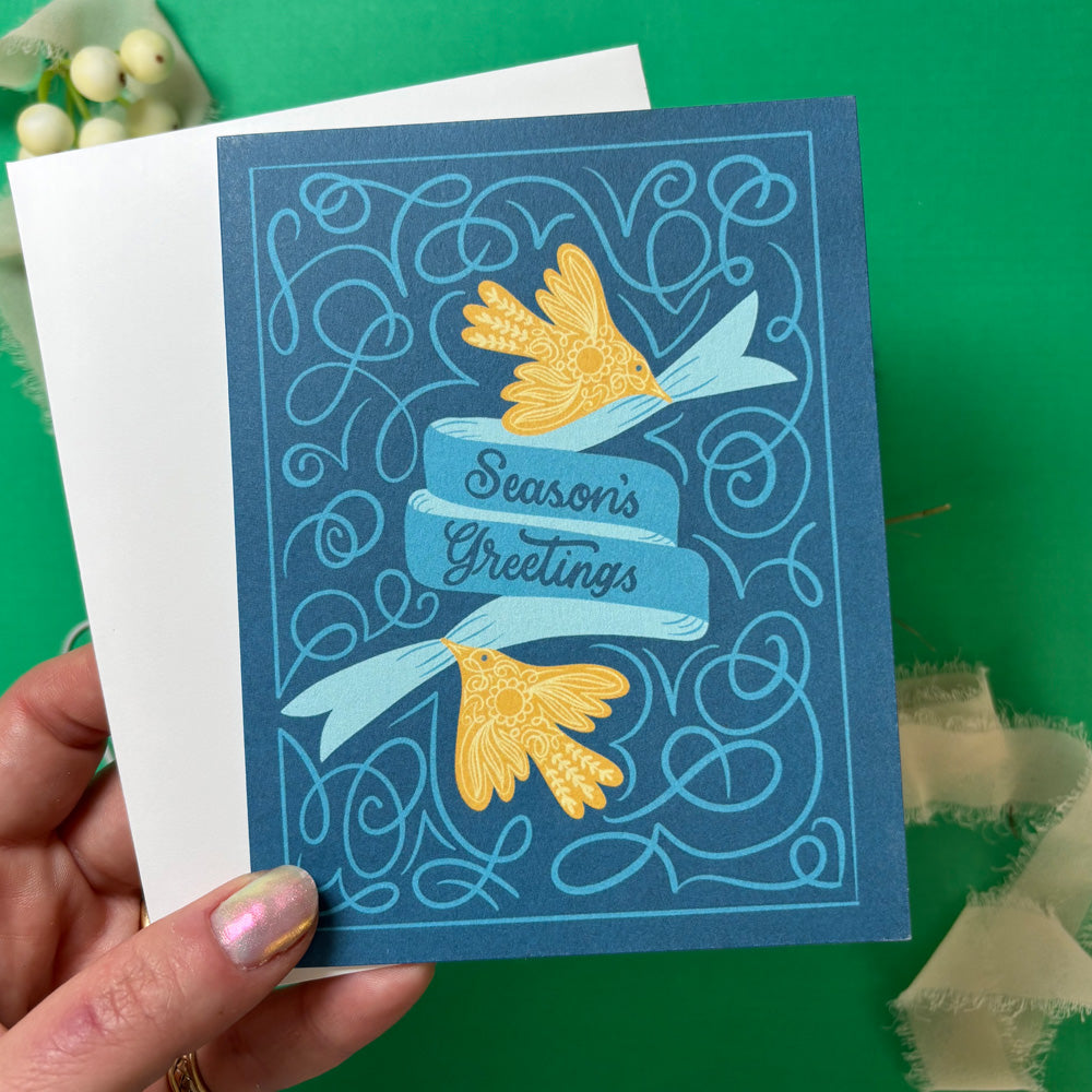 Hand holding a blue greeting card with yellow flowers and &