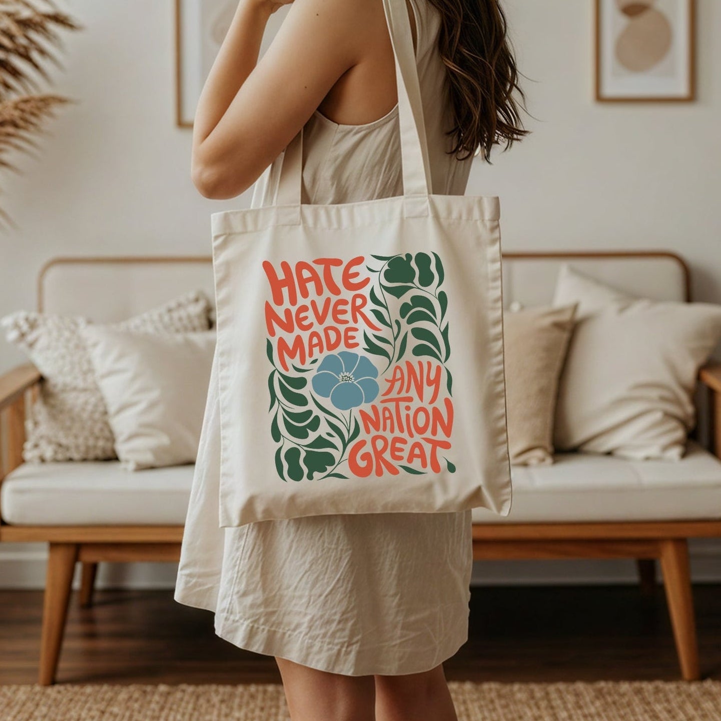 Woman holding a tote bag that reads hate never made any nation great in a living room setting