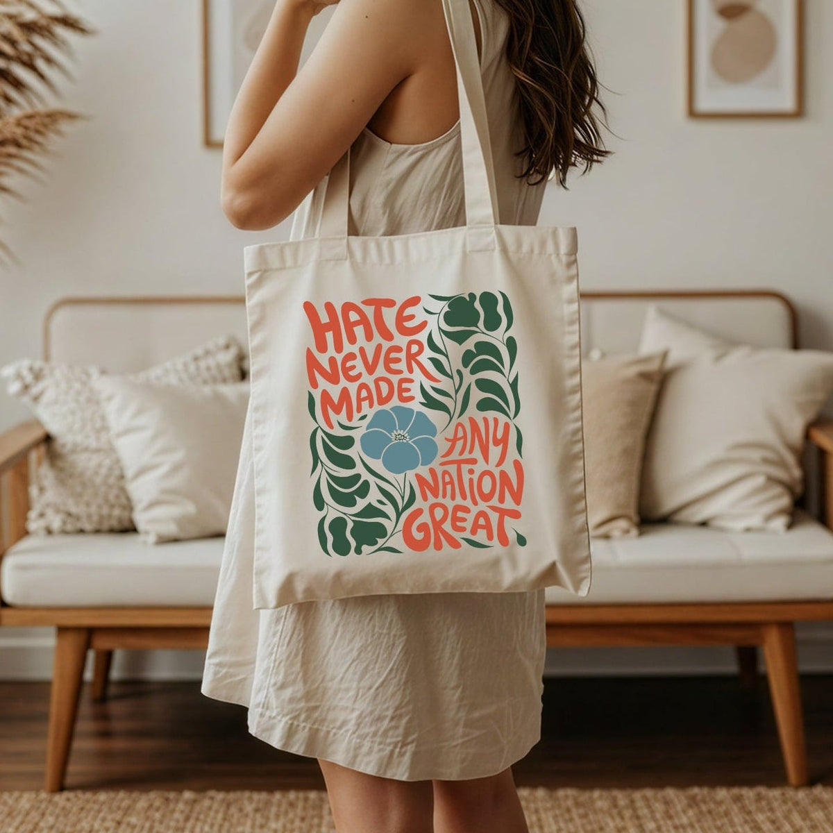 Woman holding a tote bag that reads hate never made any nation great in a living room setting