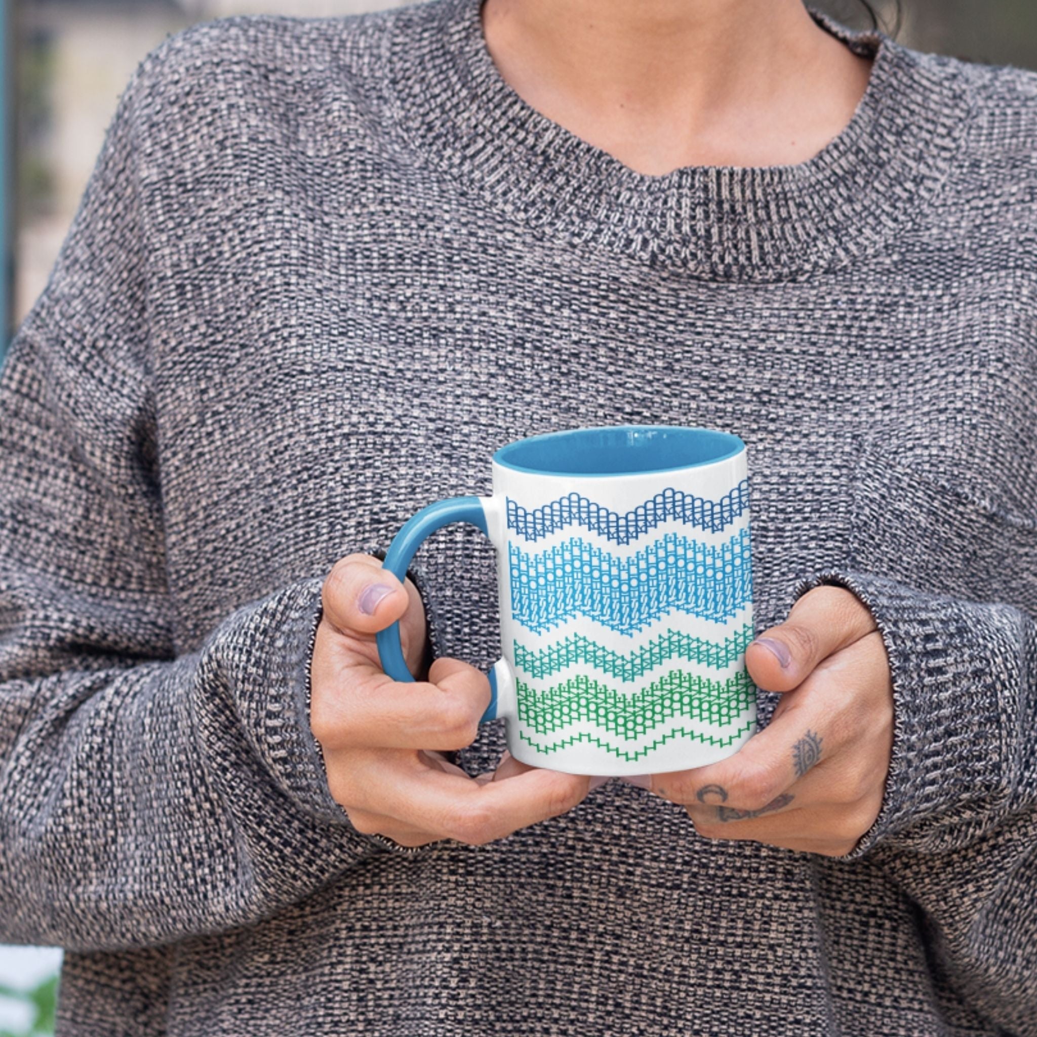 Lifestyle shot of a person in a gray marled sweater holding the Ocean Blue 11oz hidden message mug with both hands, showing the chevron pattern at chest height