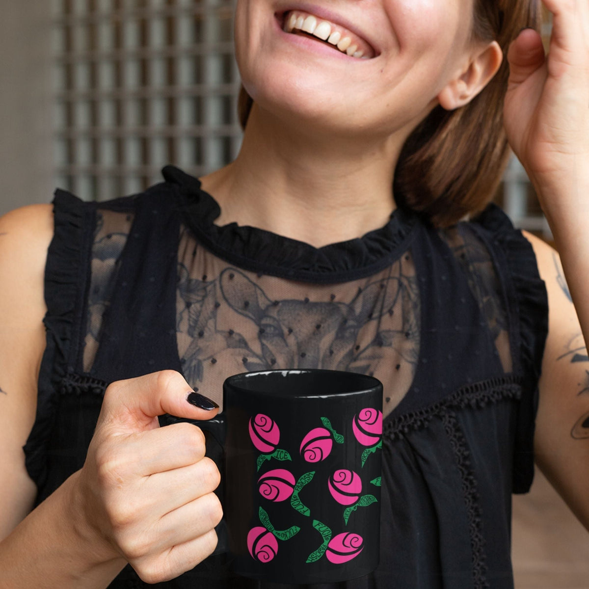 Laughing tattooed woman in black dress holding hot pink hidden message political mug, graphic rosebuds with green hand-lettered leaves on black ceramic