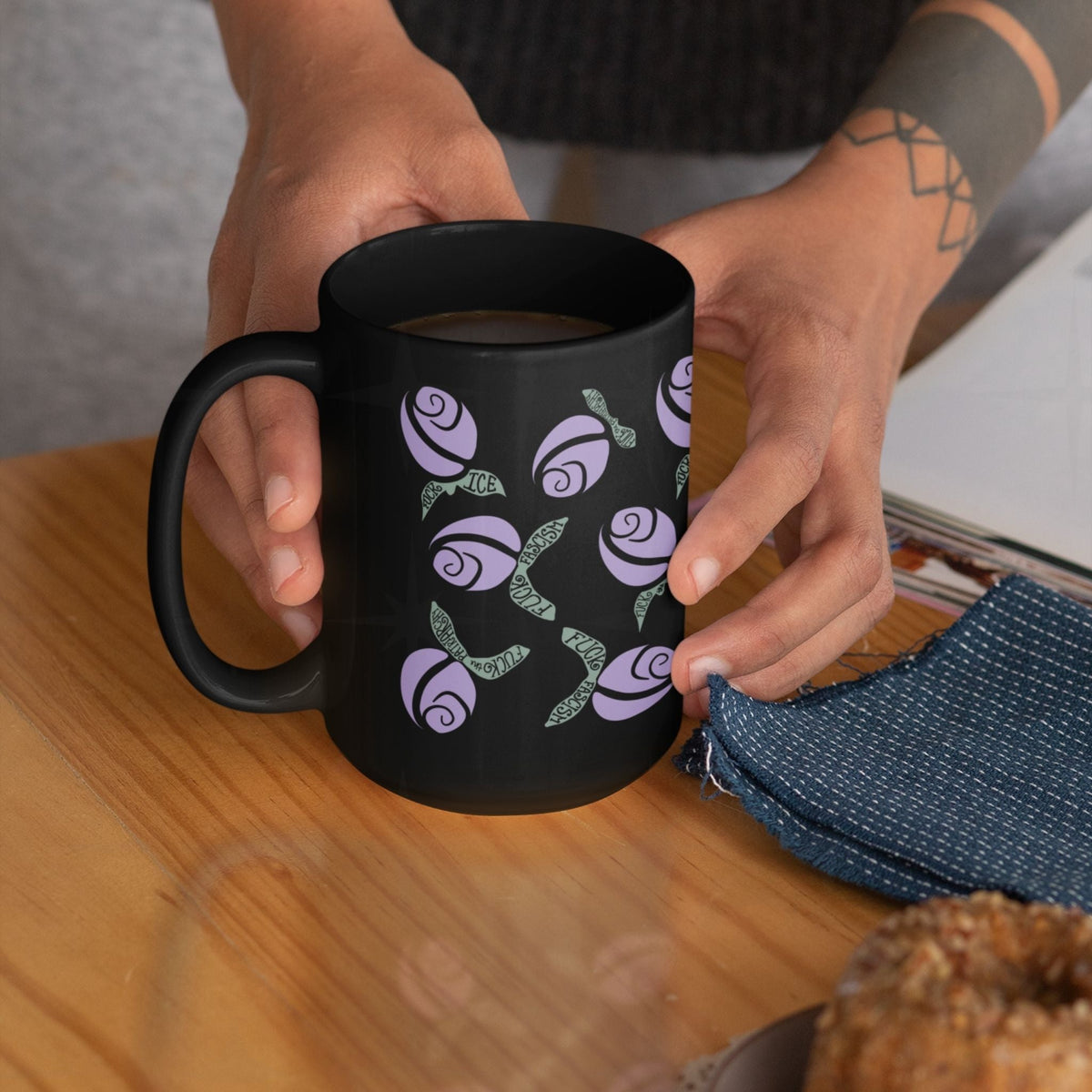 Hot pink hidden message political mug on rustic wooden table with a tea infuser being lowered in and a plate of jam toast alongside, floral protest design on black ceramic