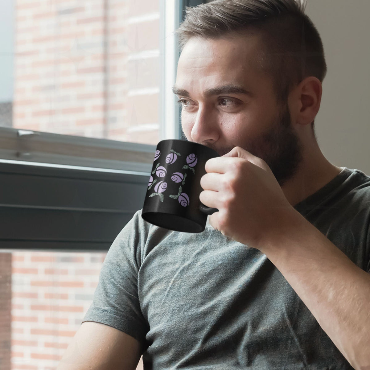 Man drinking from lilac purple hidden message political mug by a brick-view window, floral rose pattern with sage green hand-lettered leaves on black ceramic