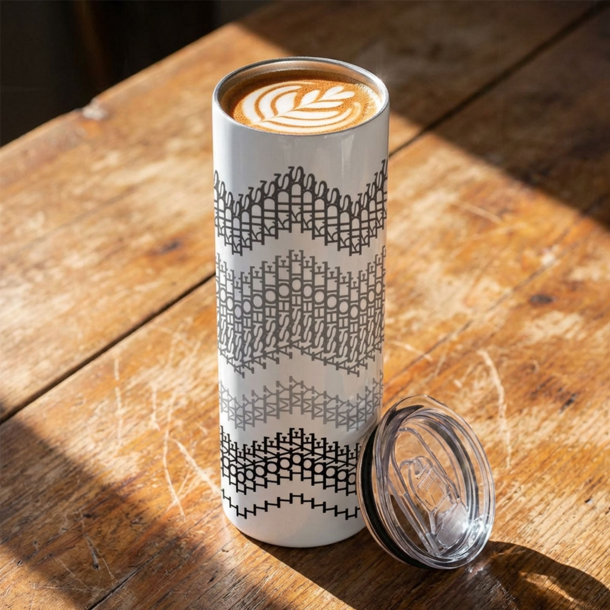 20 oz hidden message tumbler on a rustic wood surface with lid off beside it, gray stripes colorway — black, gray, and charcoal embroidery stripe chevron bands on white body with latte art visible inside