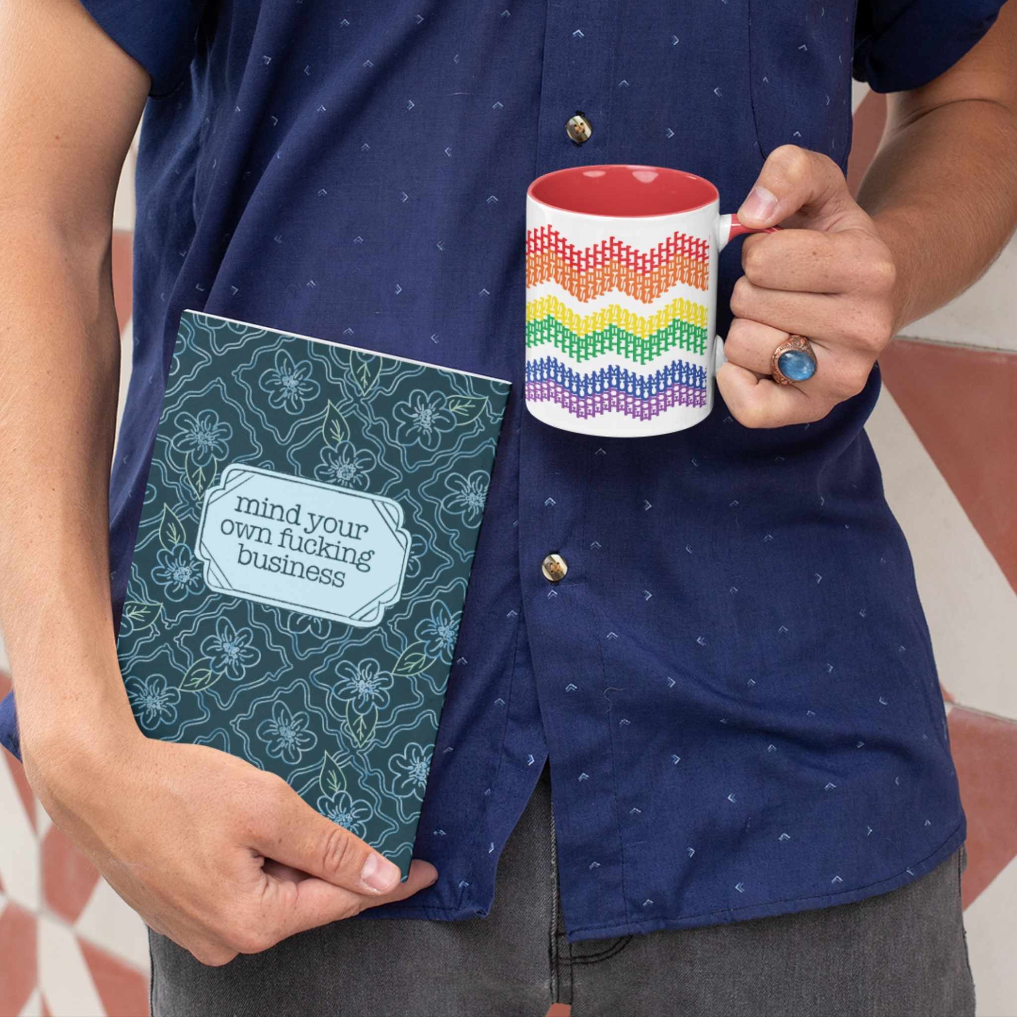 Person holding rainbow hidden profanity accent mug alongside "mind your own fucking business" journal