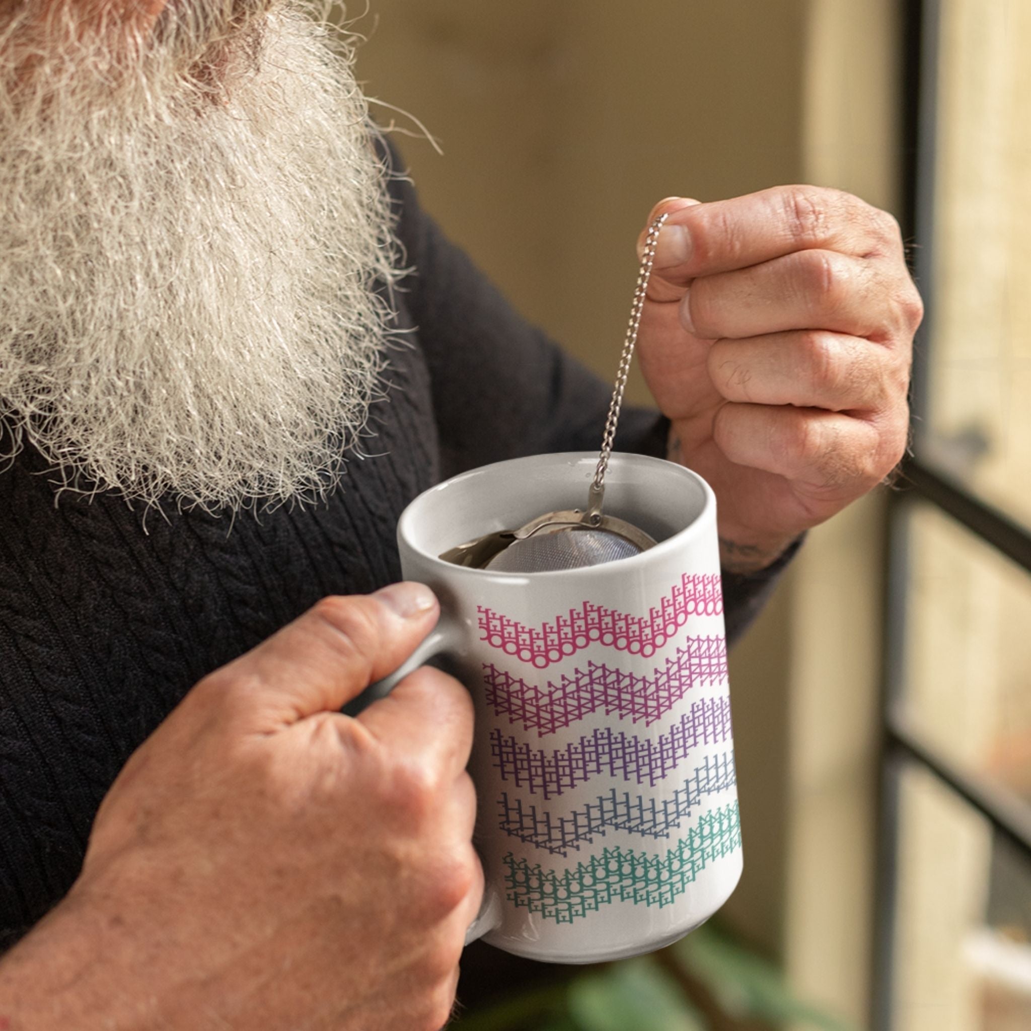 Older bearded man steeping tea with a ball infuser in bright stripes hidden profanity chevron mug in hot pink purple and teal