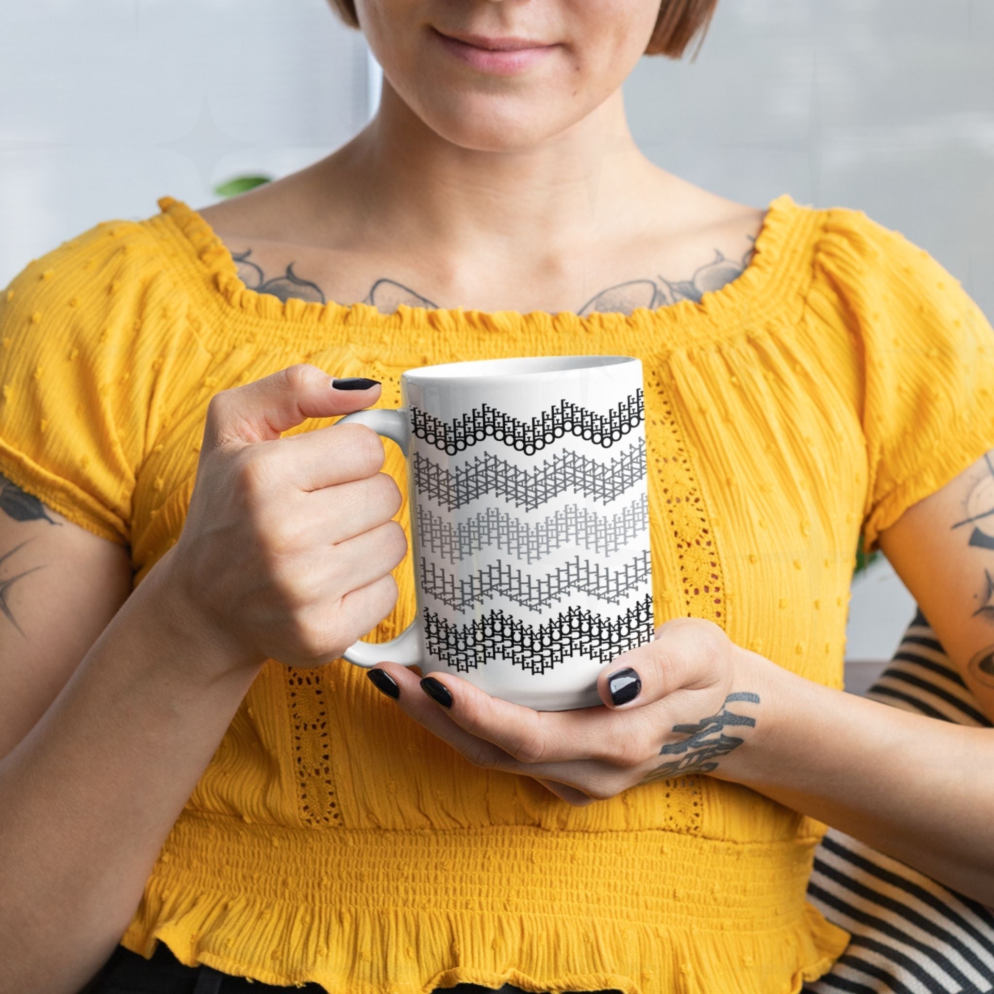 Tattooed woman in yellow eyelet blouse holding gray stripes hidden profanity chevron mug with both hands