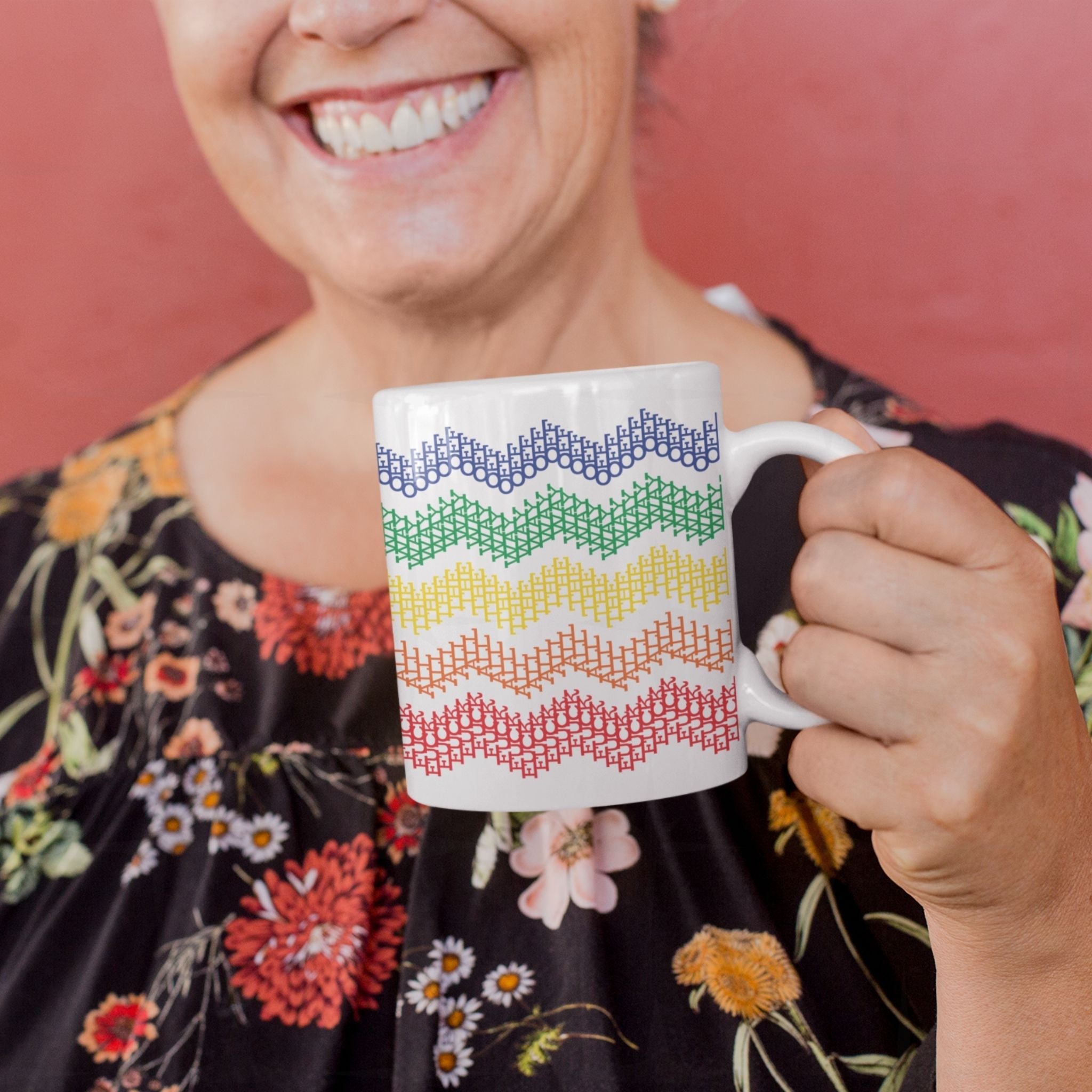 Smiling woman in black floral blouse holding rainbow stripes hidden profanity chevron mug against pink background